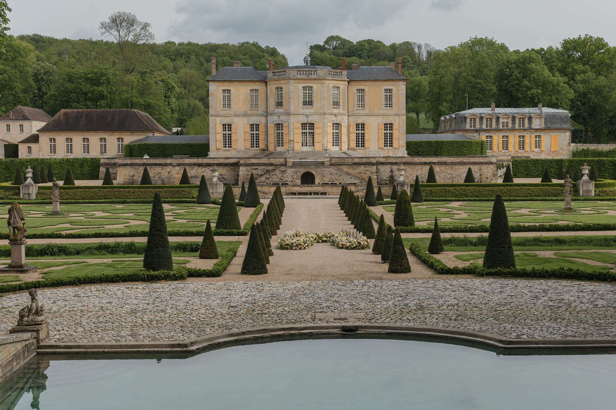 Classical chateau with conical topiaries, ornamental pool, and blush floral arrangement on central path