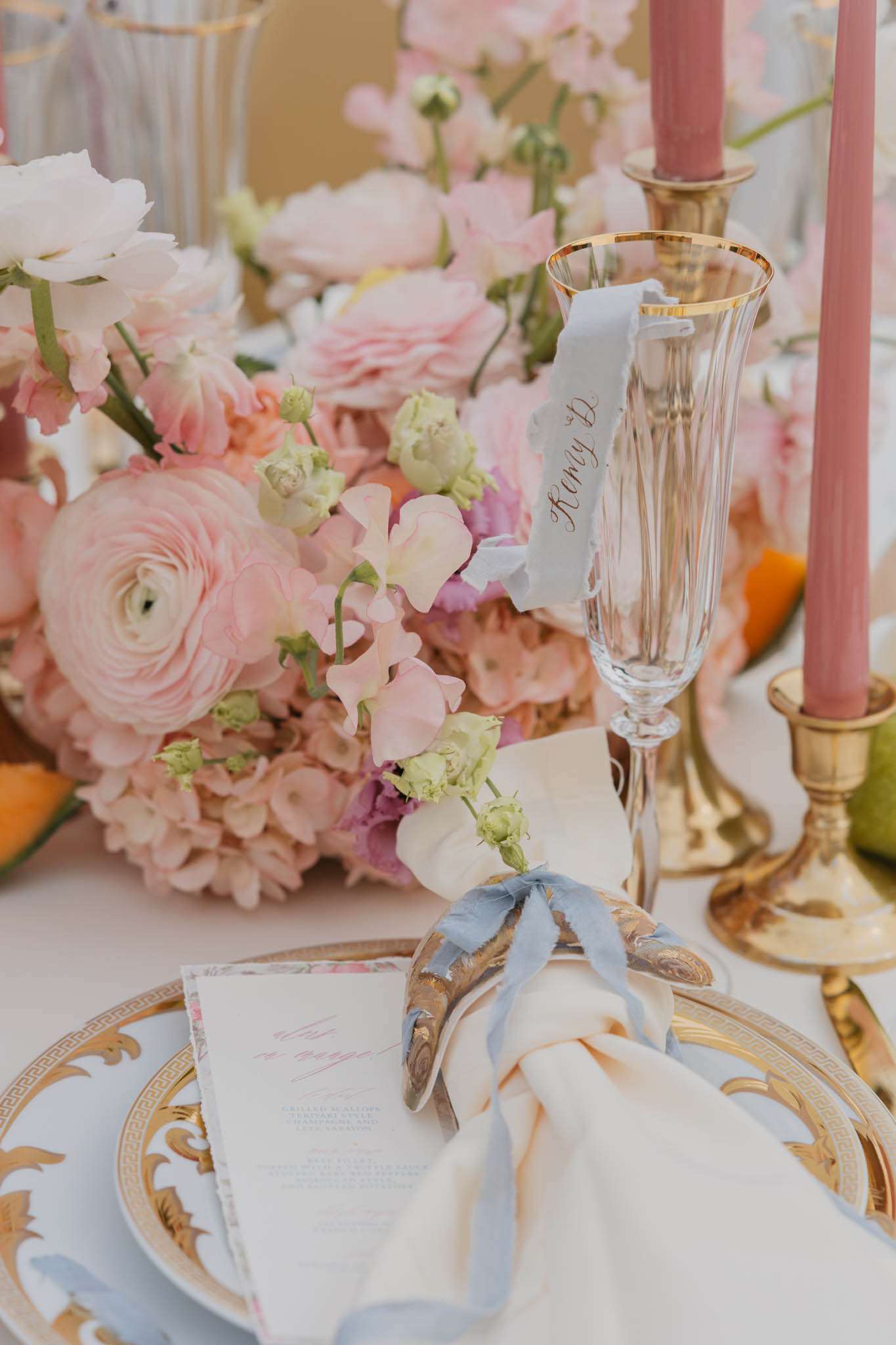 Classic French place setting with gold-rimmed china, calligraphy card, blush ranunculus, and dusty blue ribbon