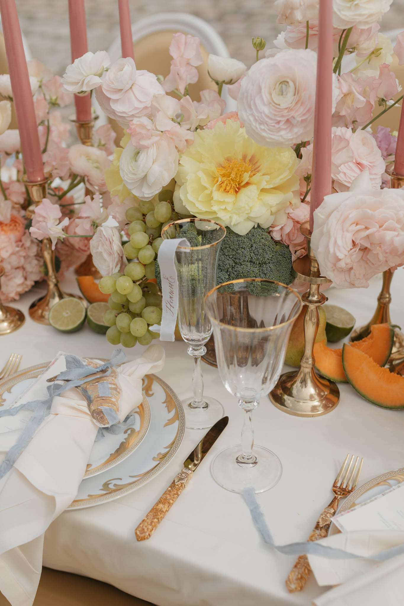 Baroque china place setting with blush roses, fresh fruit, dusty rose candles, and gold-handled cutlery