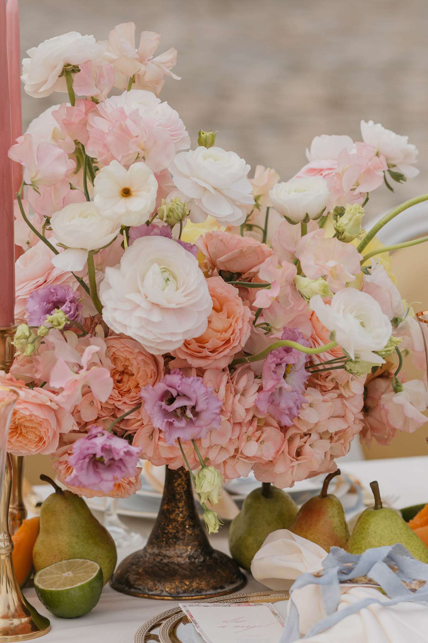 Reception centerpiece with peach roses, pink sweet peas, and purple lisianthus in bronze pedestal vase