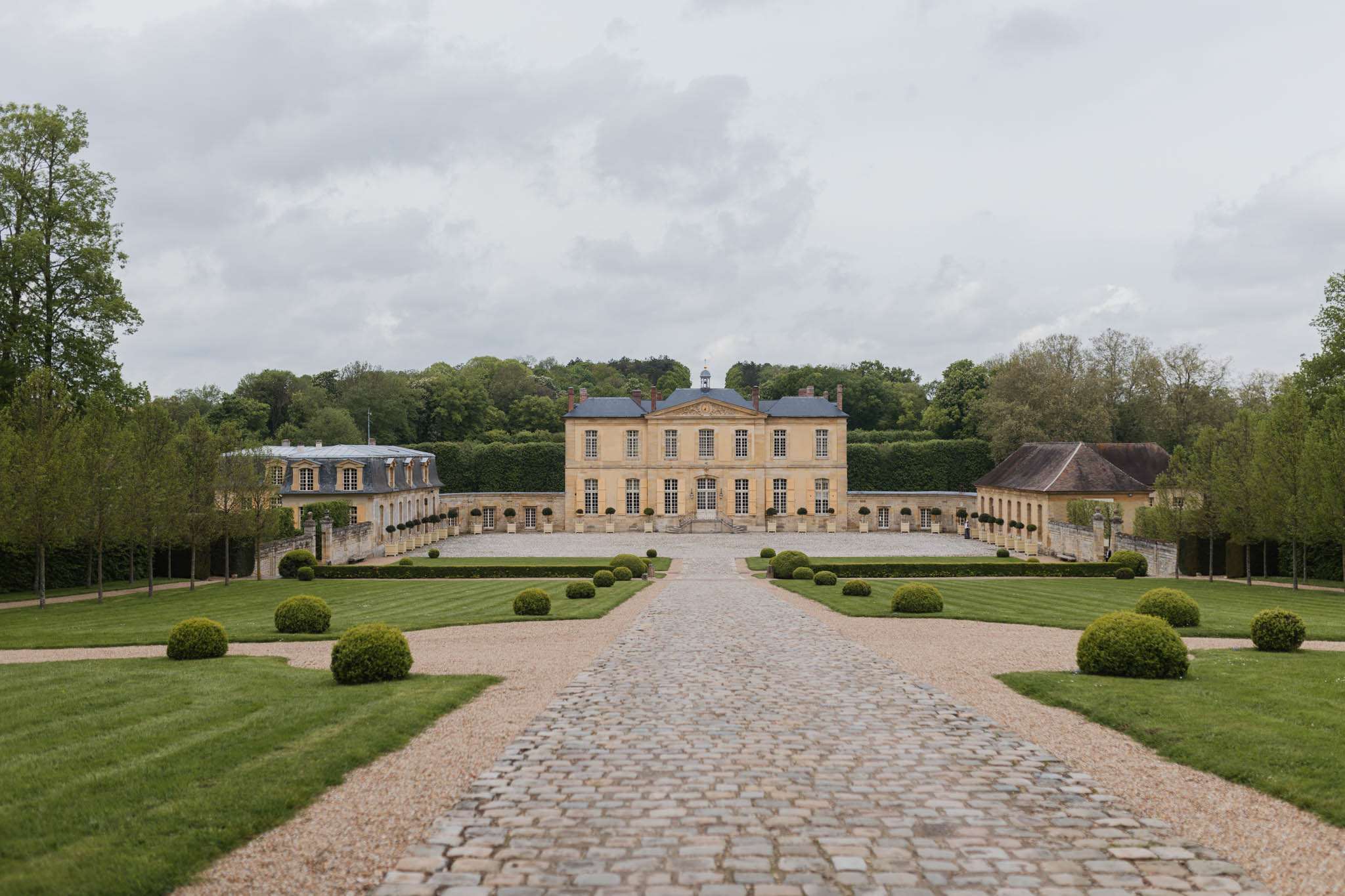 Symmetrical view of honey-colored stone chateau with mansard roof, blue dome, and boxwood parterre