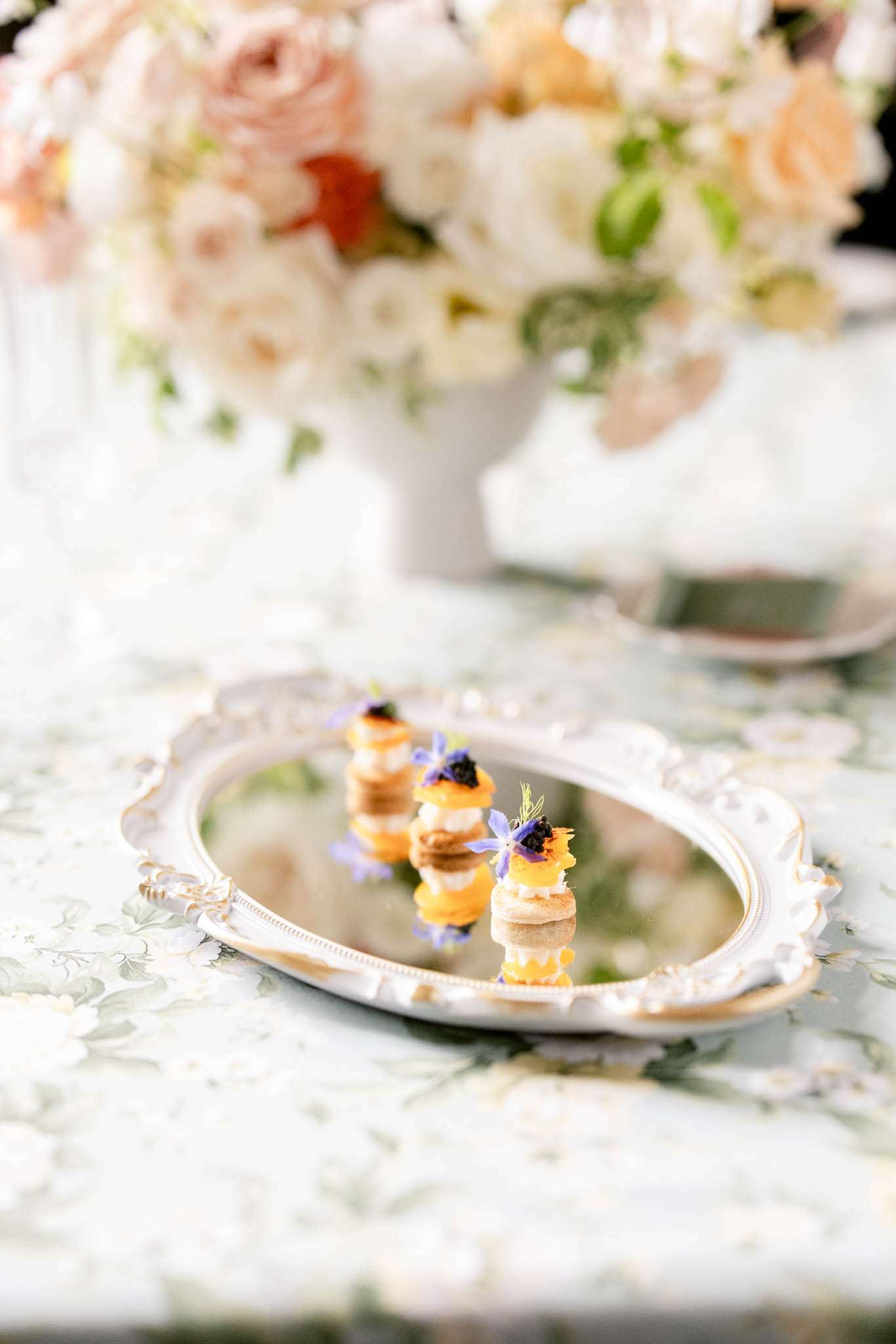 Stacked canape bites with caviar and borage flowers on silver mirror tray at reception