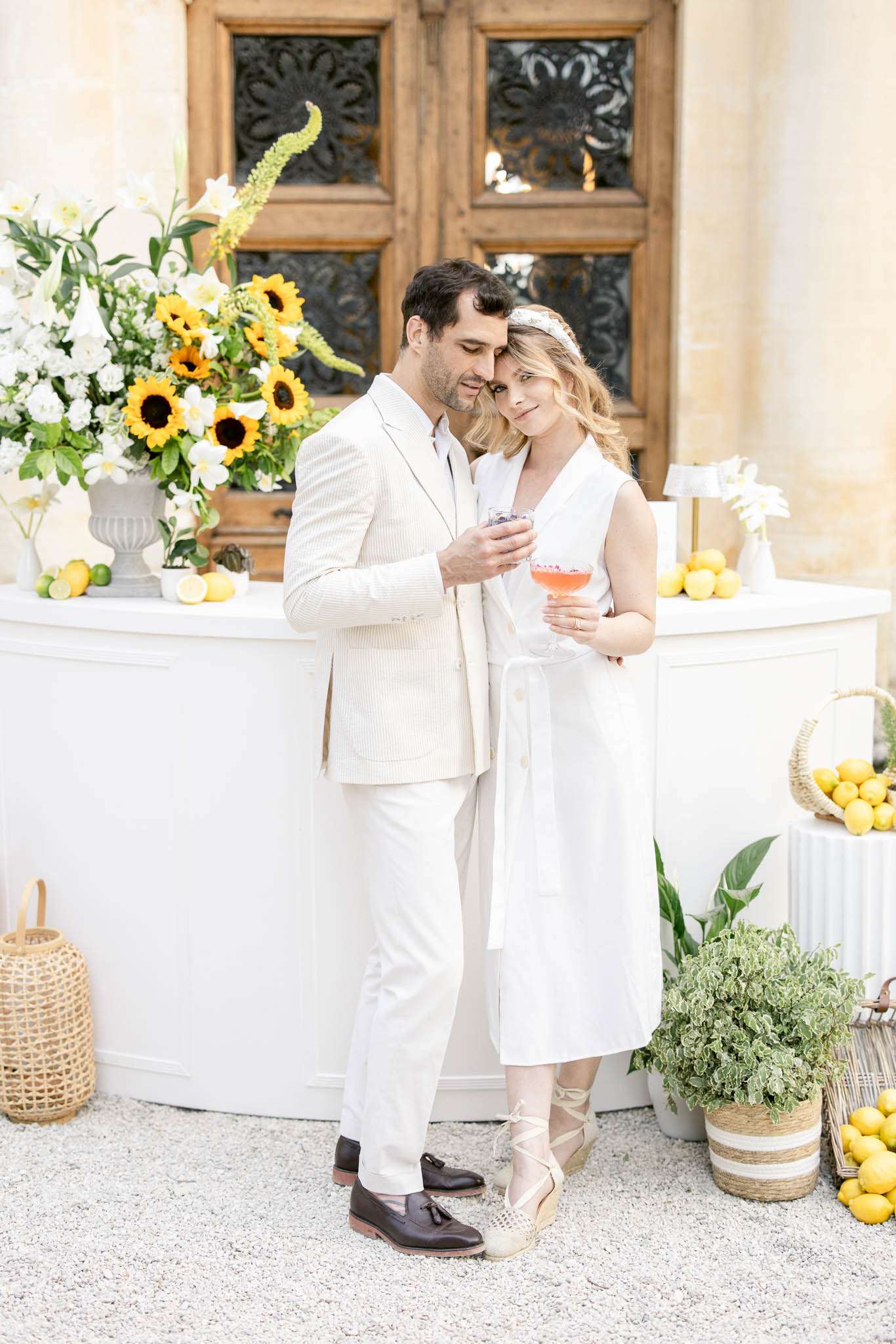 Bride and groom at cocktail bar with pink drinks, sunflower arrangement, and lemon decor at French chateau