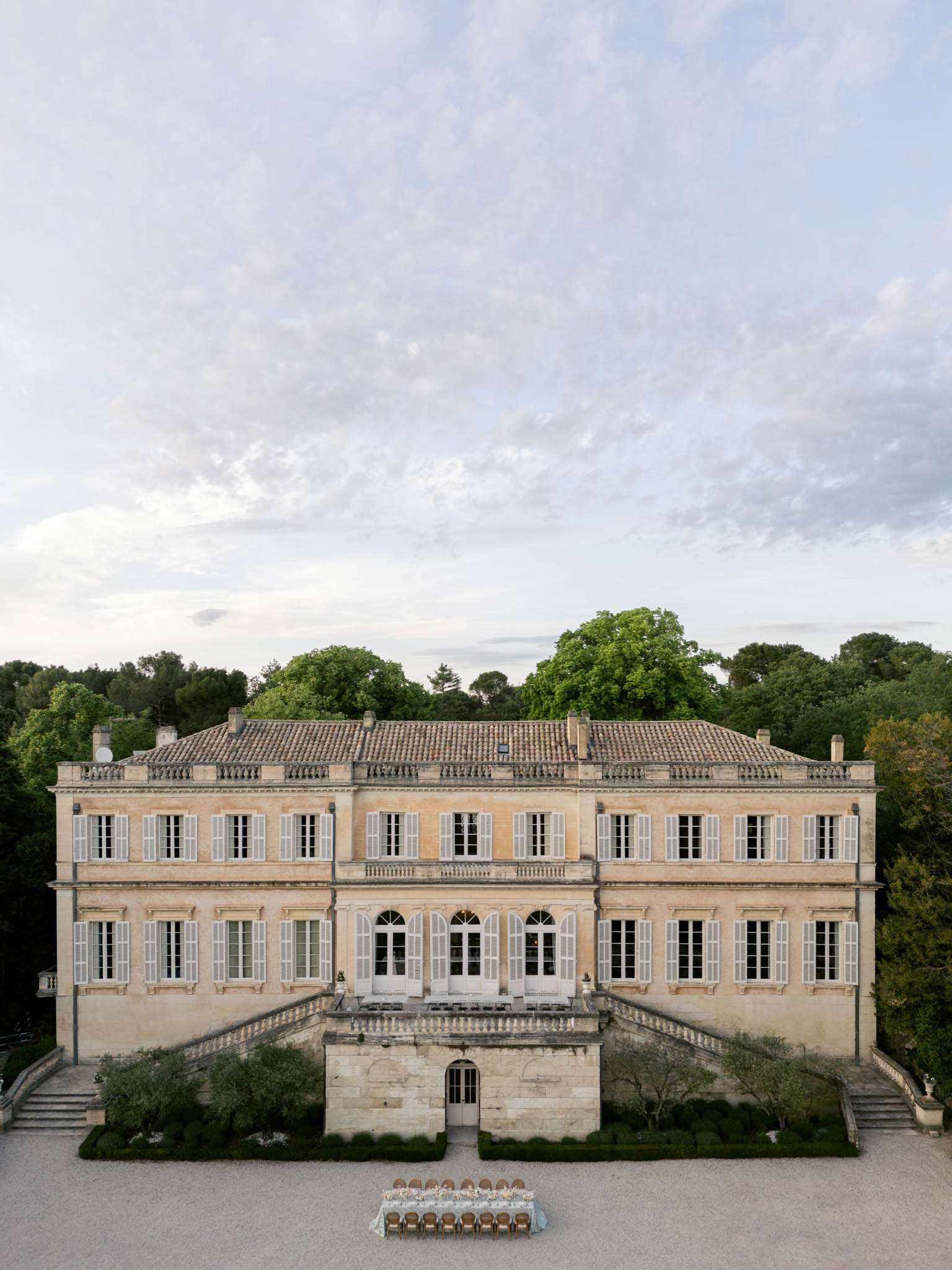 Aerial view of a honey-stone French chateau with long reception table set on the gravel forecourt