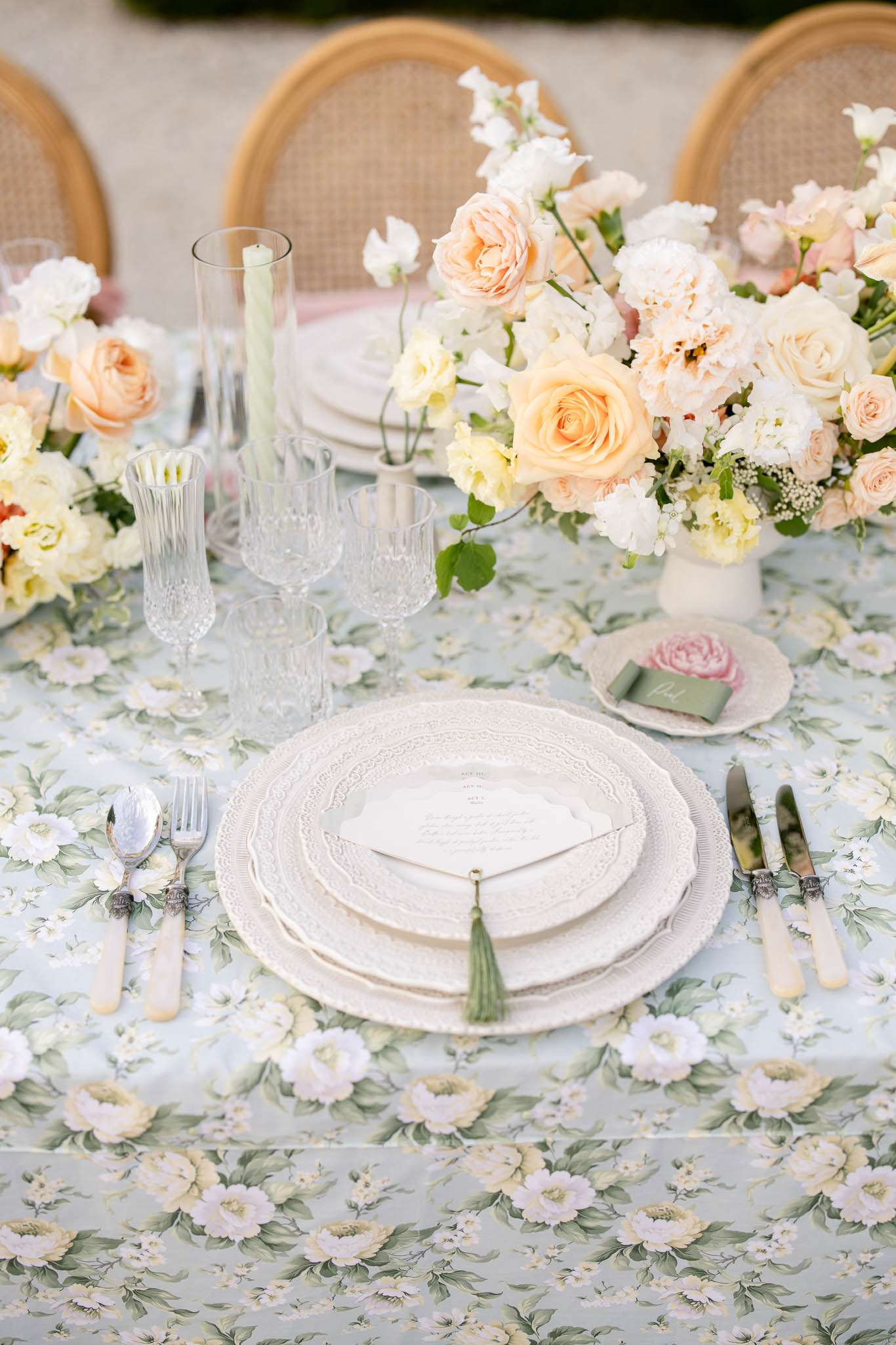 Lace-edged plates on sage floral linen with peach rose centrepiece, mother-of-pearl cutlery, and tassel menu
