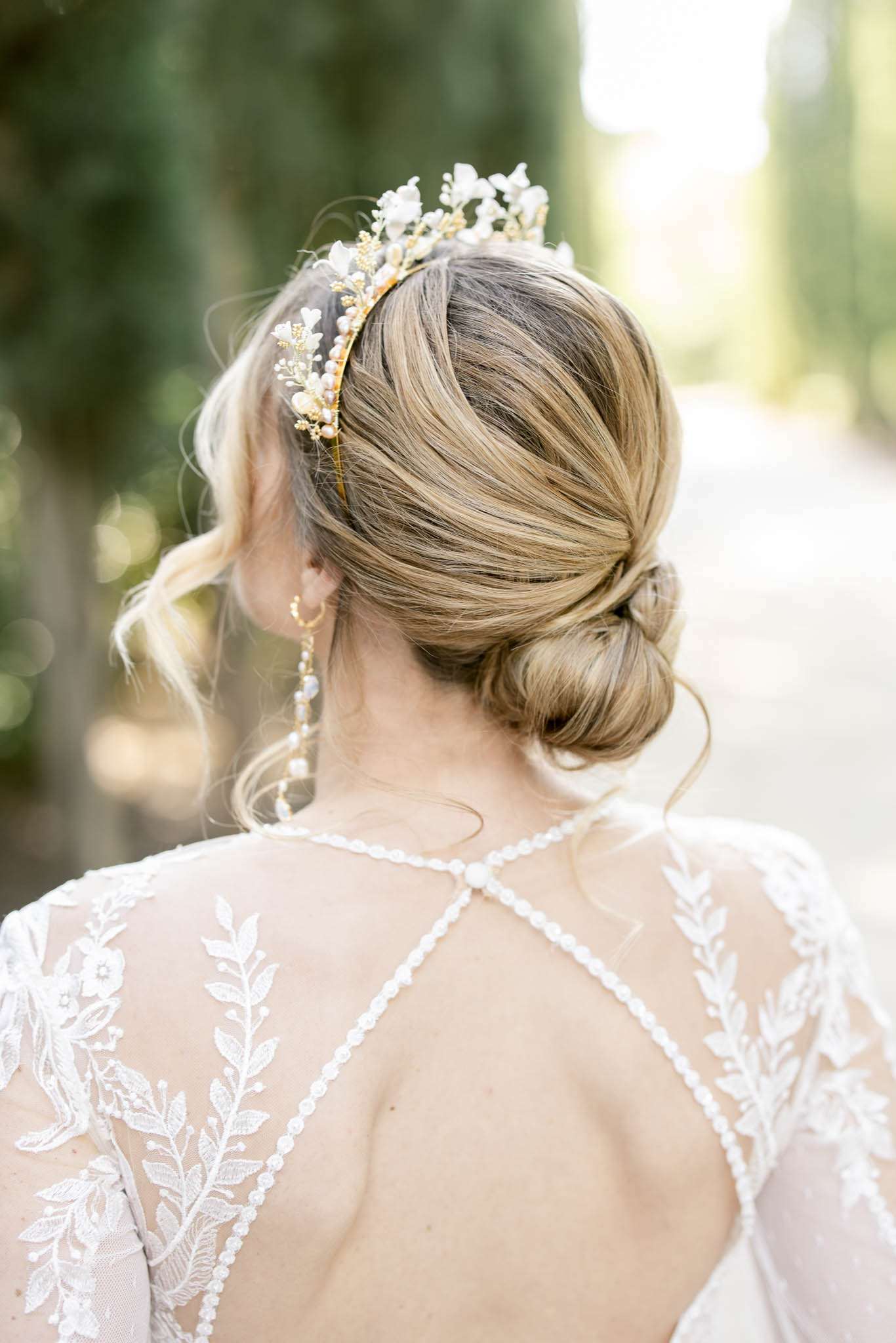 Close-up of bridal updo with gold floral crown pearl earring and lace open-back dress from behind