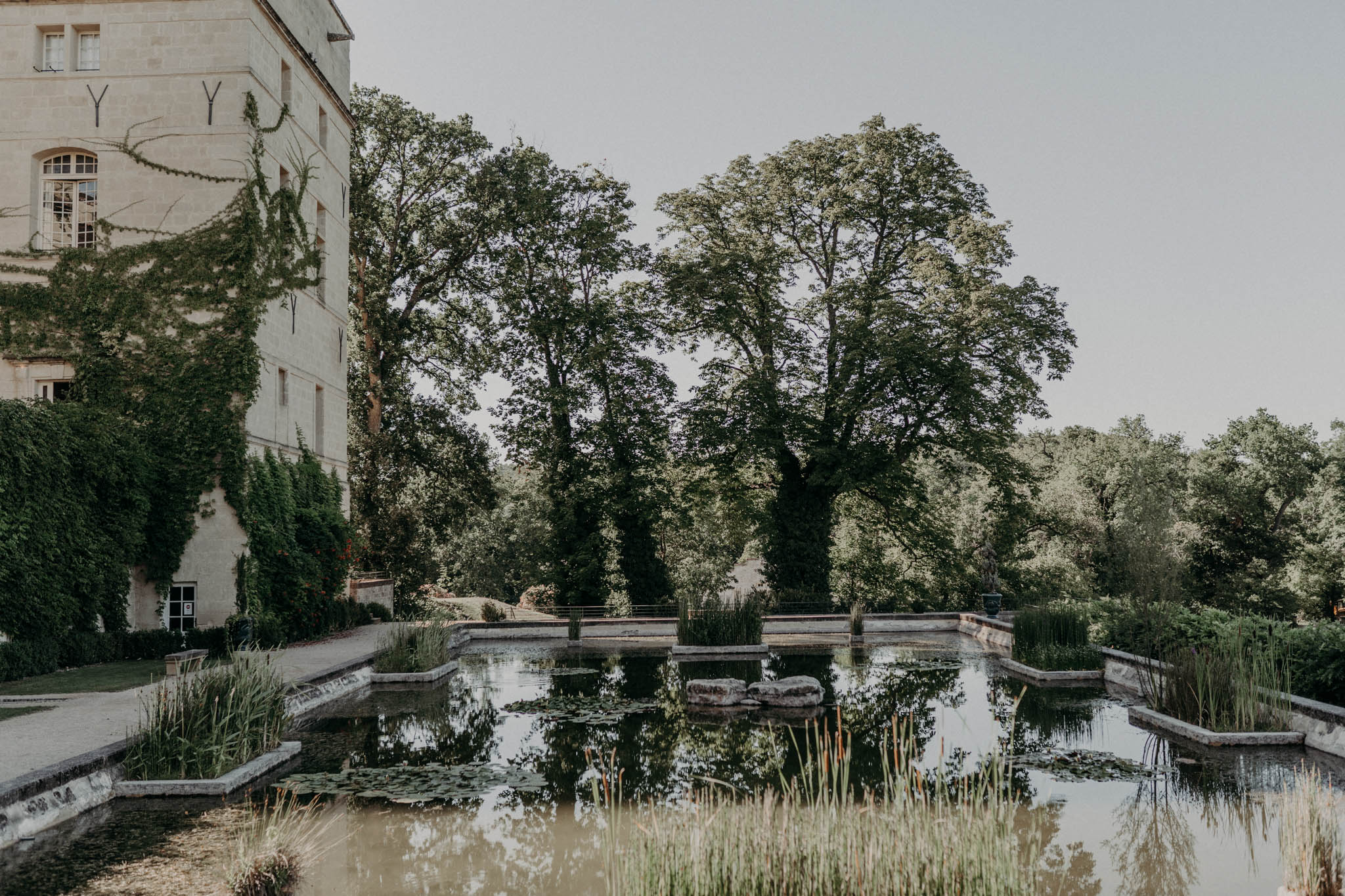 French chateau exterior with rectangular ornamental pond, lily pads, and ivy-covered limestone facade