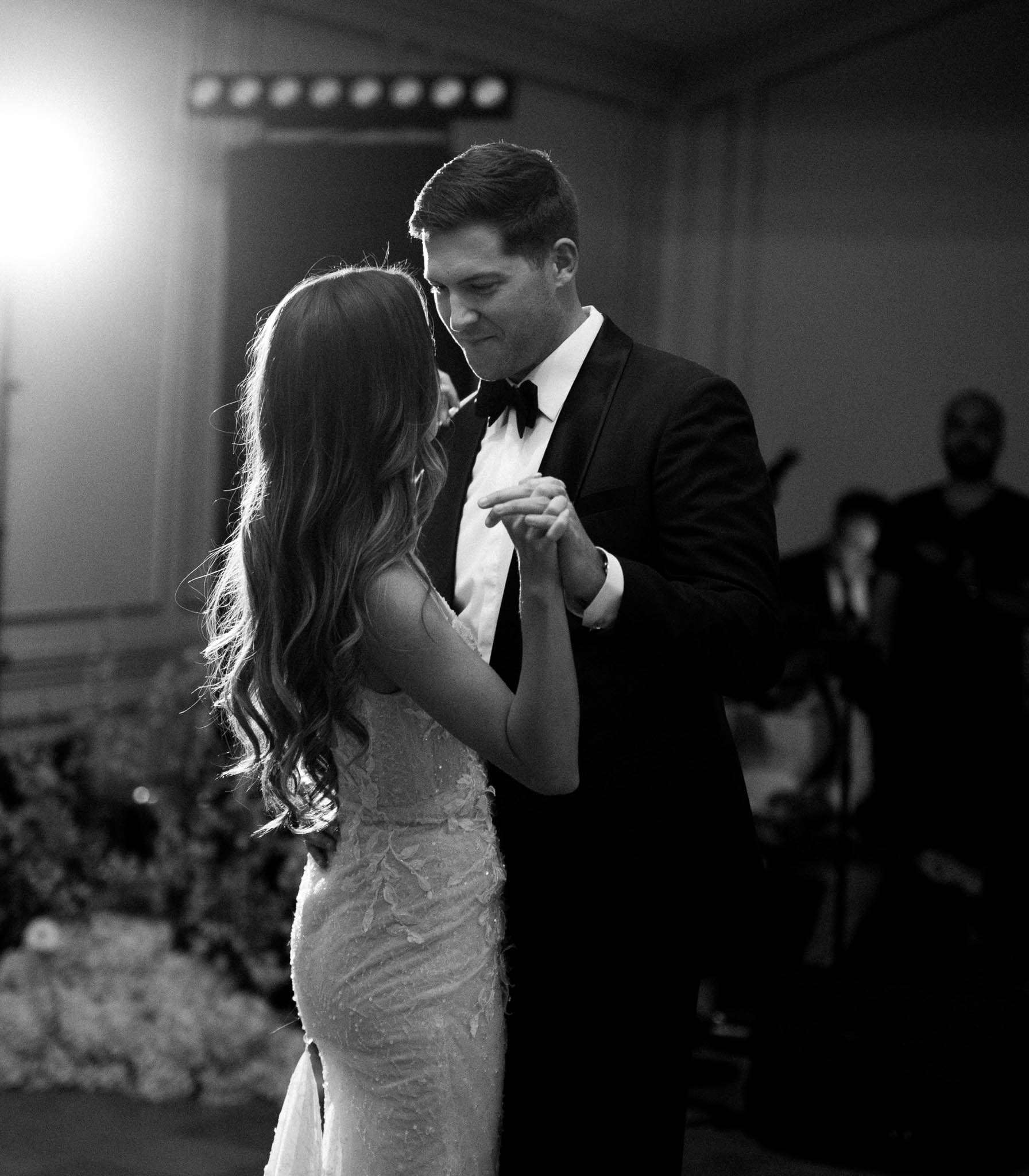 Black and white first dance in beaded gown and tuxedo with floral installation and stage lights