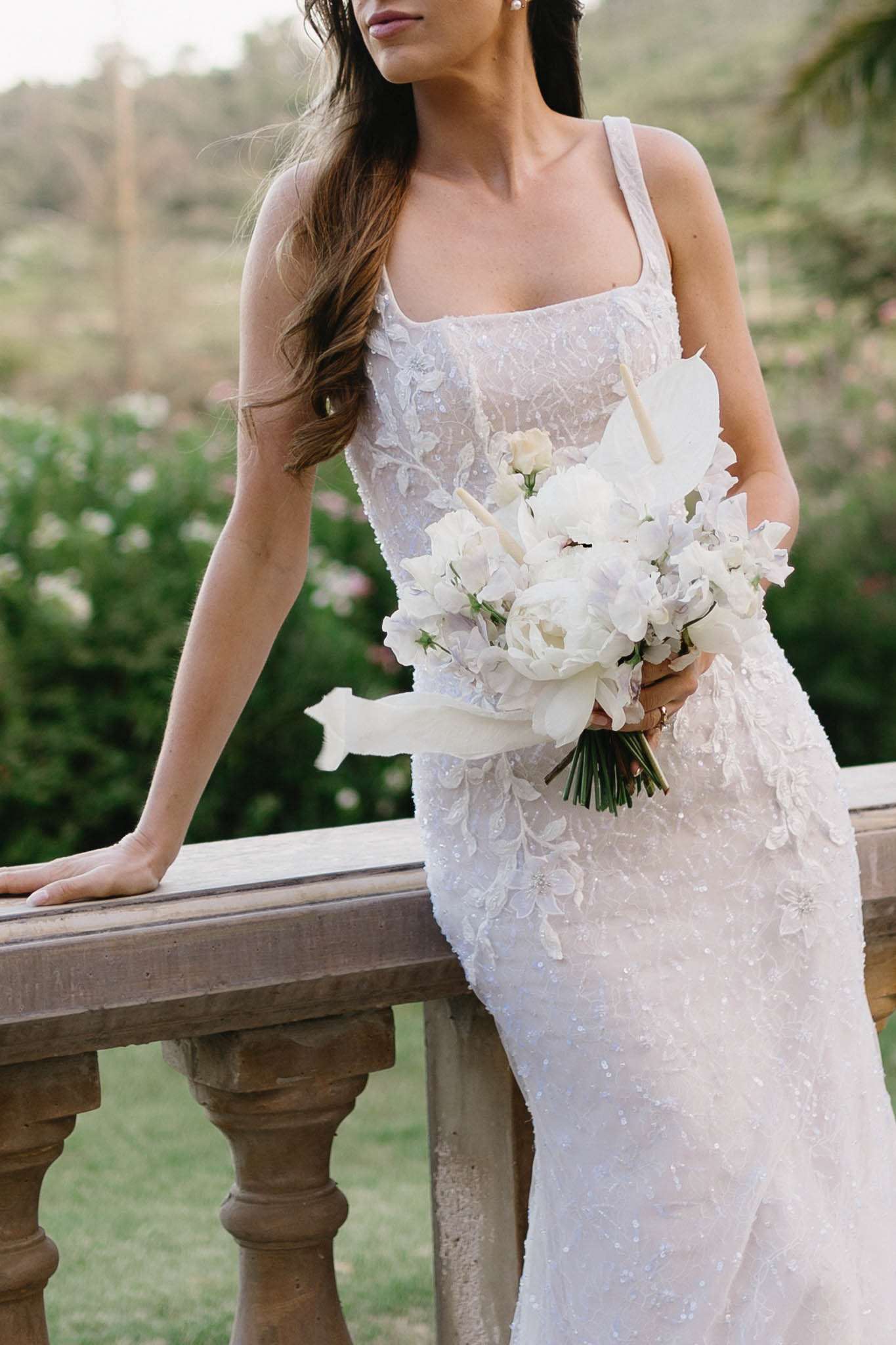 Bride in iridescent sequin floral applique gown holding white peony and sweet pea bouquet on stone terrace