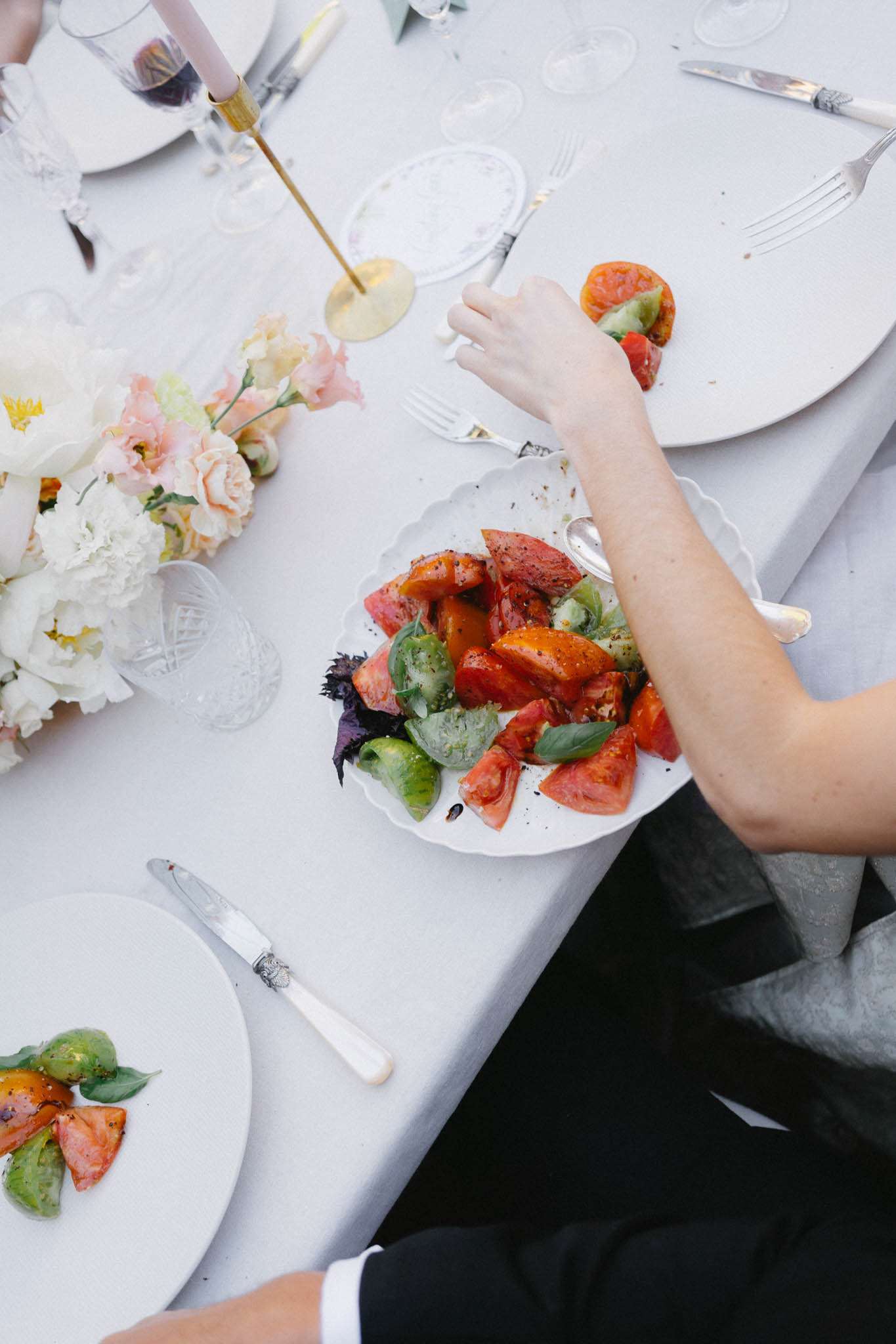 Overhead view of heirloom tomato salad on scallop plates with peony centerpiece and gold candlesticks