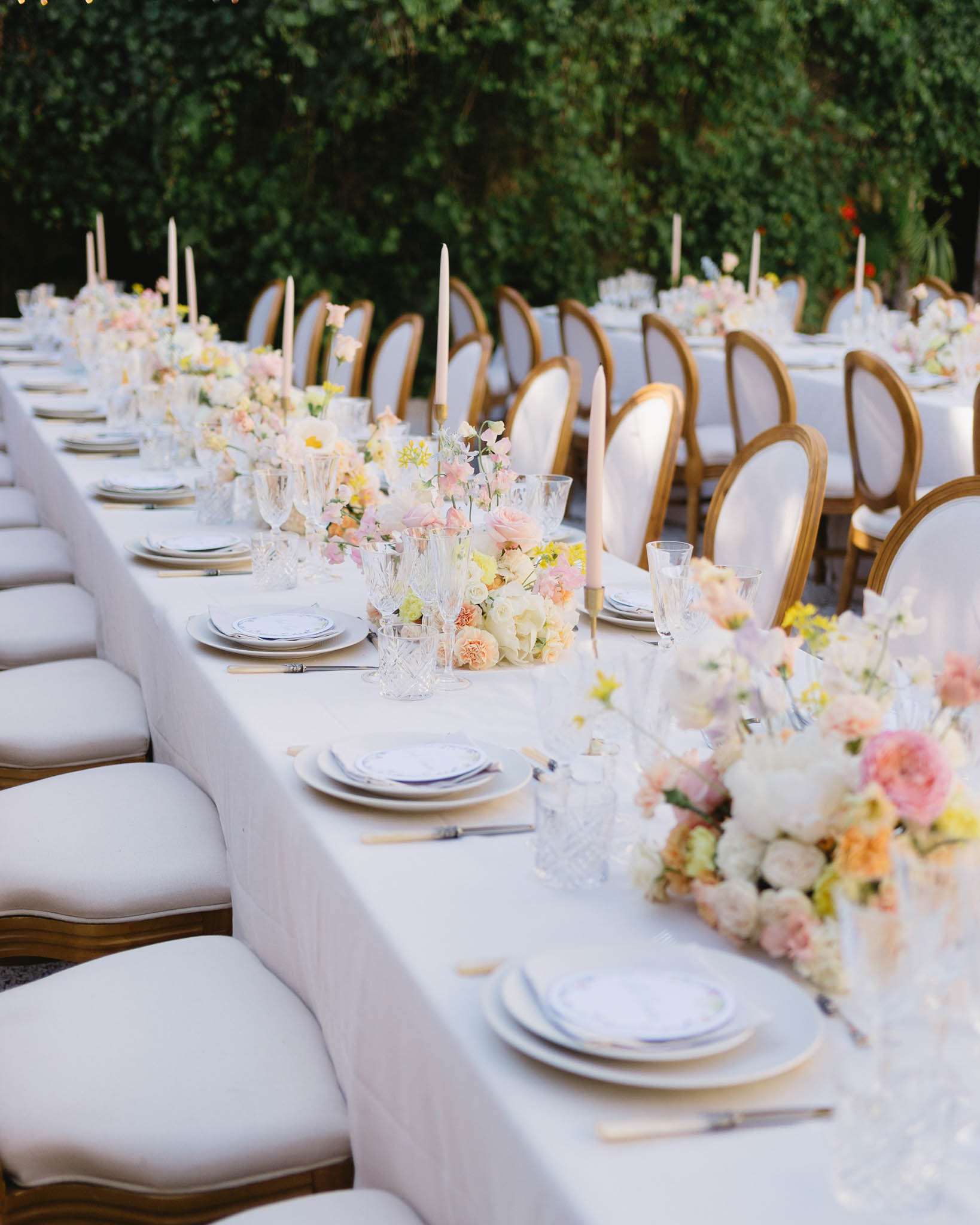 Outdoor reception table with pastel floral centerpieces, gold flatware, crystal glasses, and Louis XVI chairs