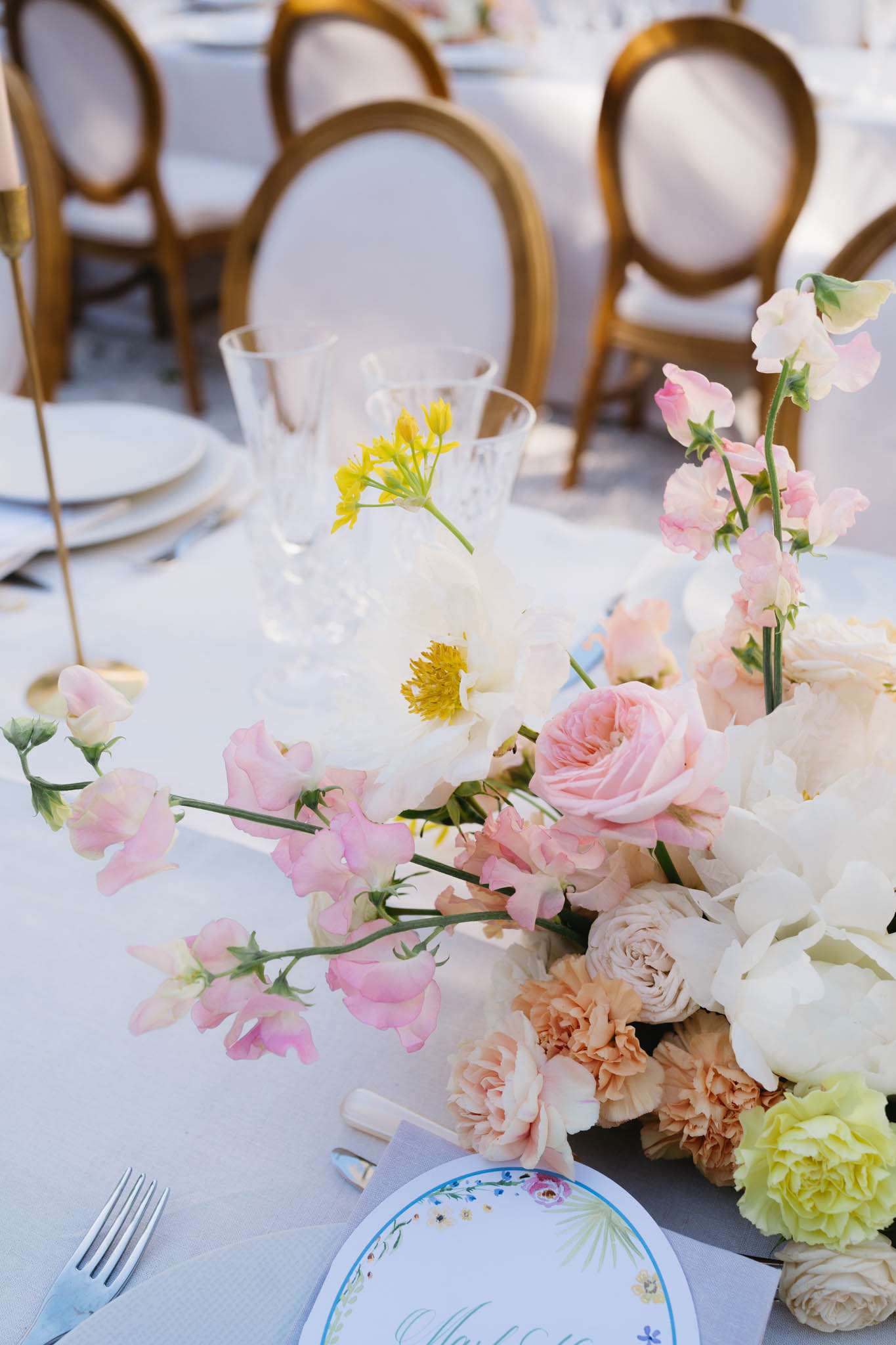 Centrepiece of blush roses, white peonies, and peach carnations with floral charger and crystal glassware