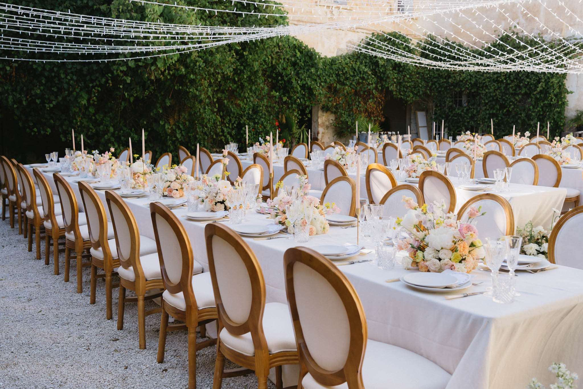 Courtyard reception with gold medallion chairs, ivory peony centerpieces, and fairy light canopy