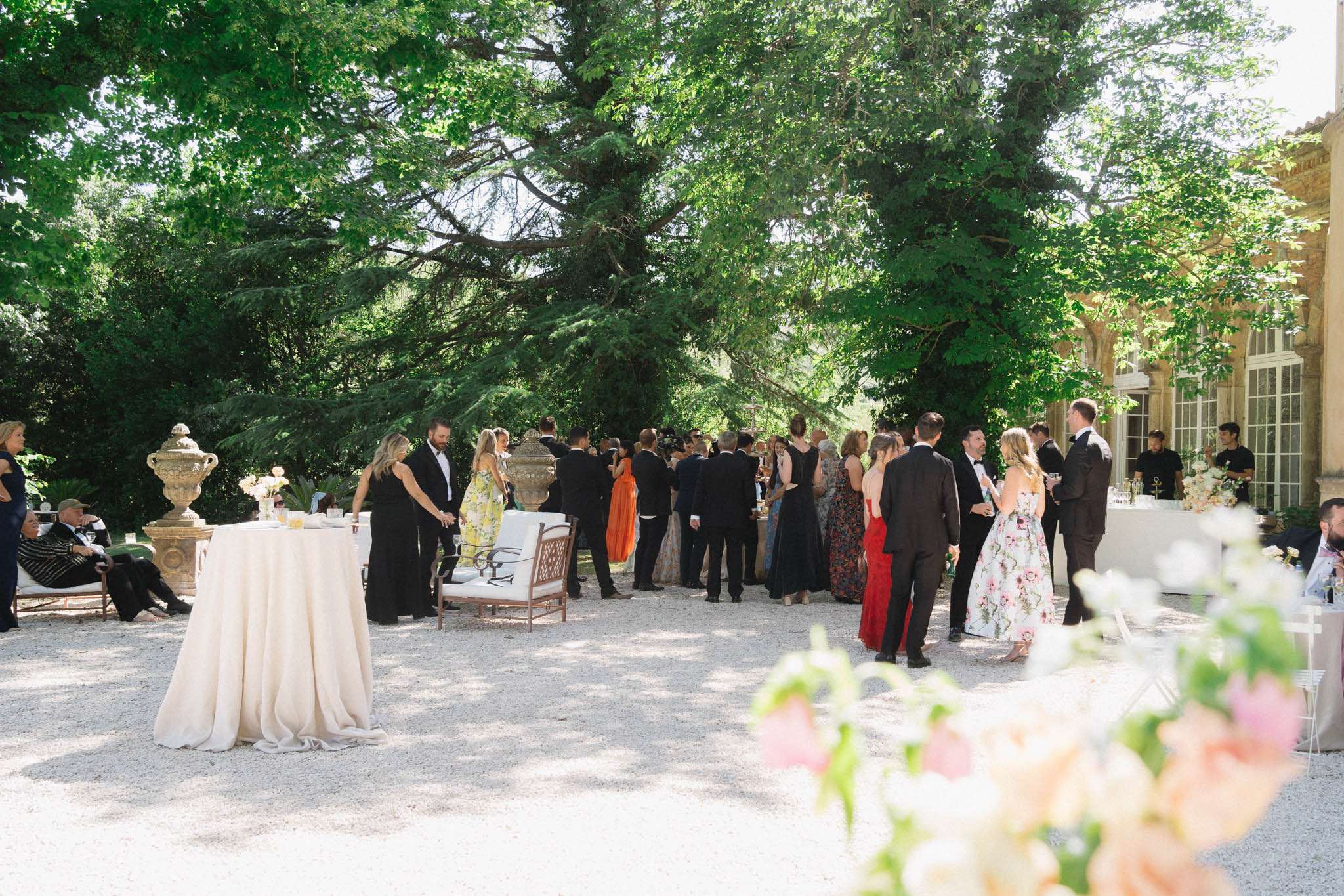 Guests mingle on gravel forecourt during cocktail hour beside French chateau with cocktail tables and florals