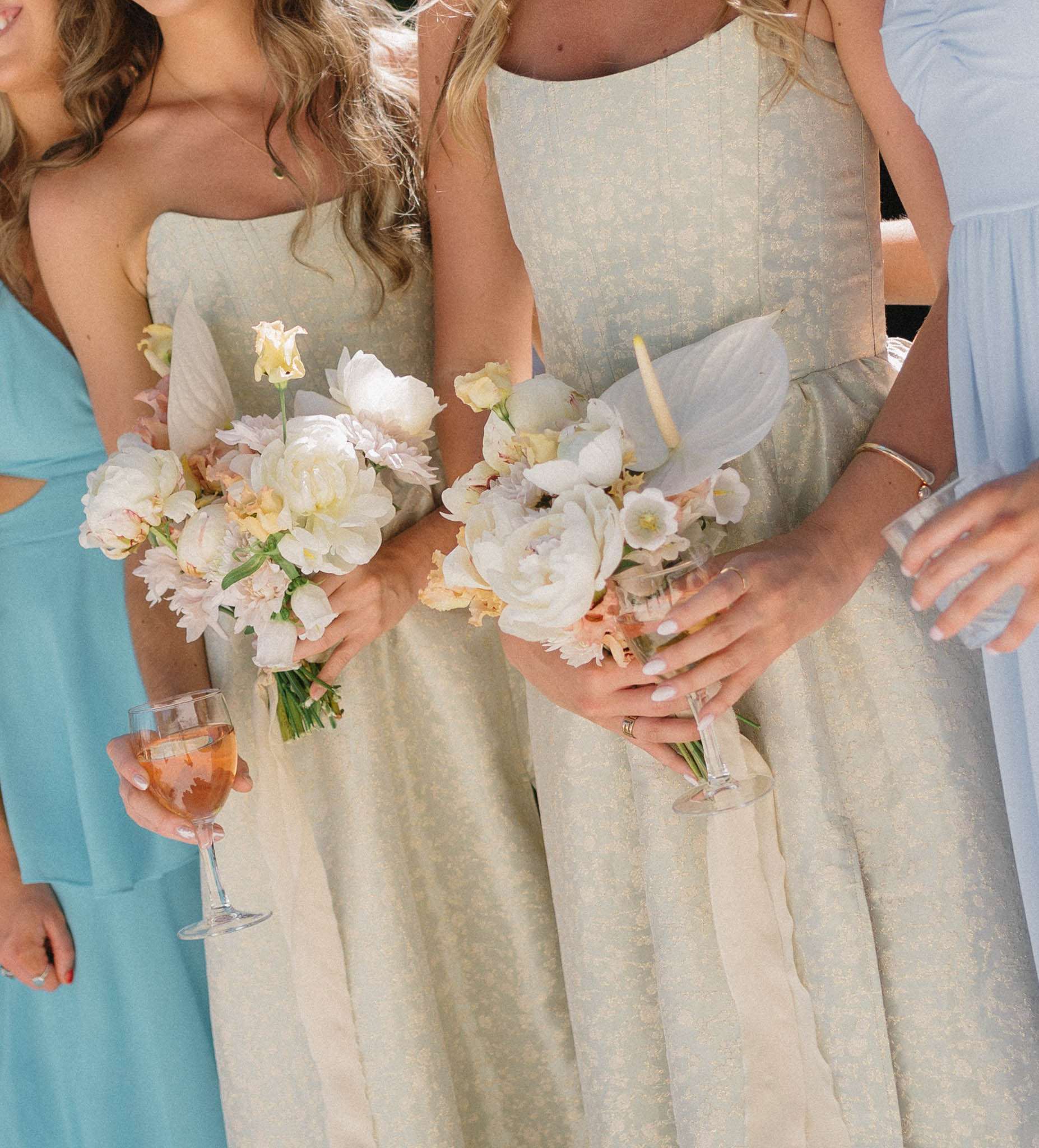 Bridesmaids in mix-and-match sage green and pastel dresses holding white peony and blush garden-style bouquets