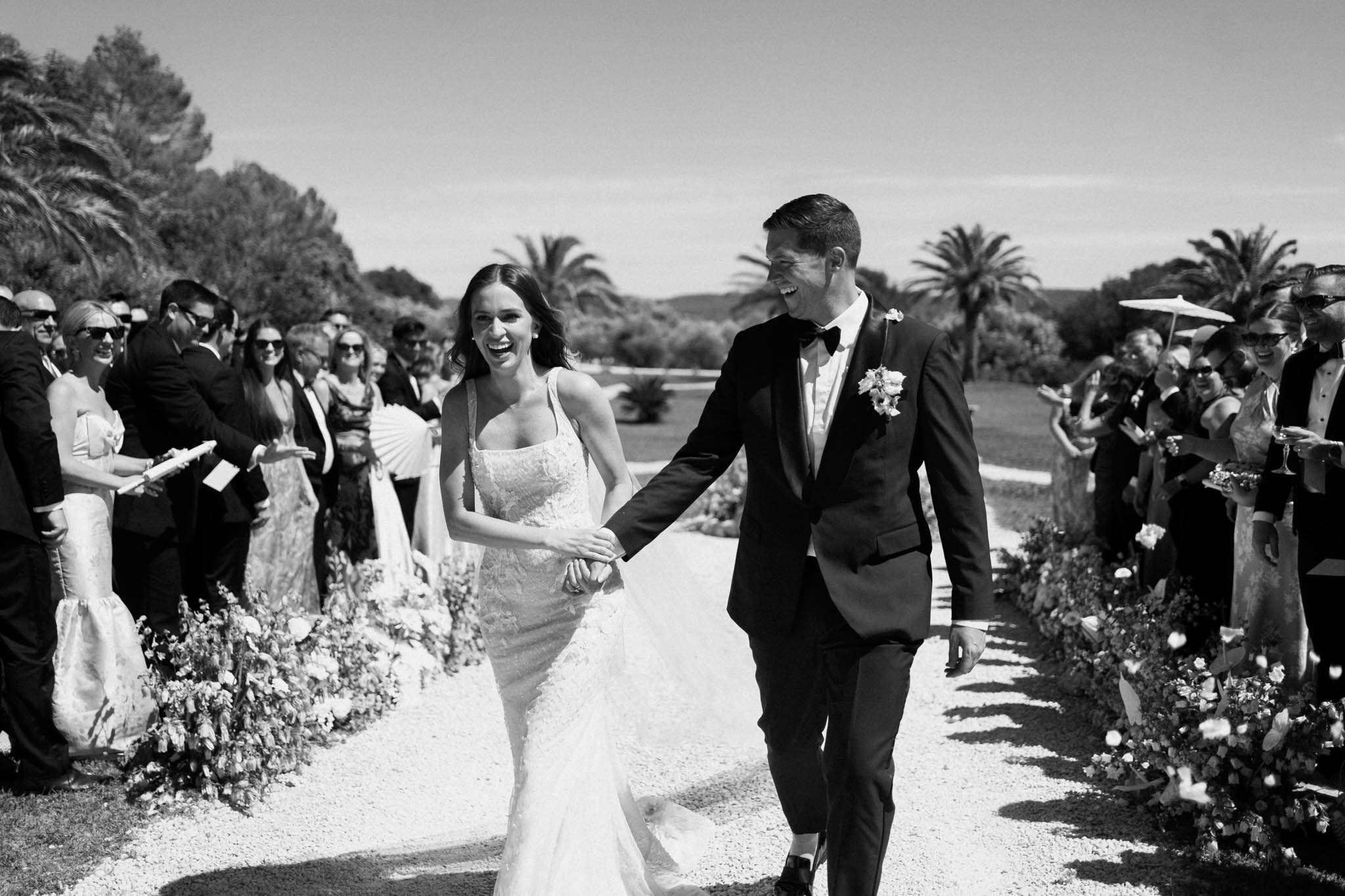 Black and white recessional with laughing bride and groom passing cheering guests with parasols