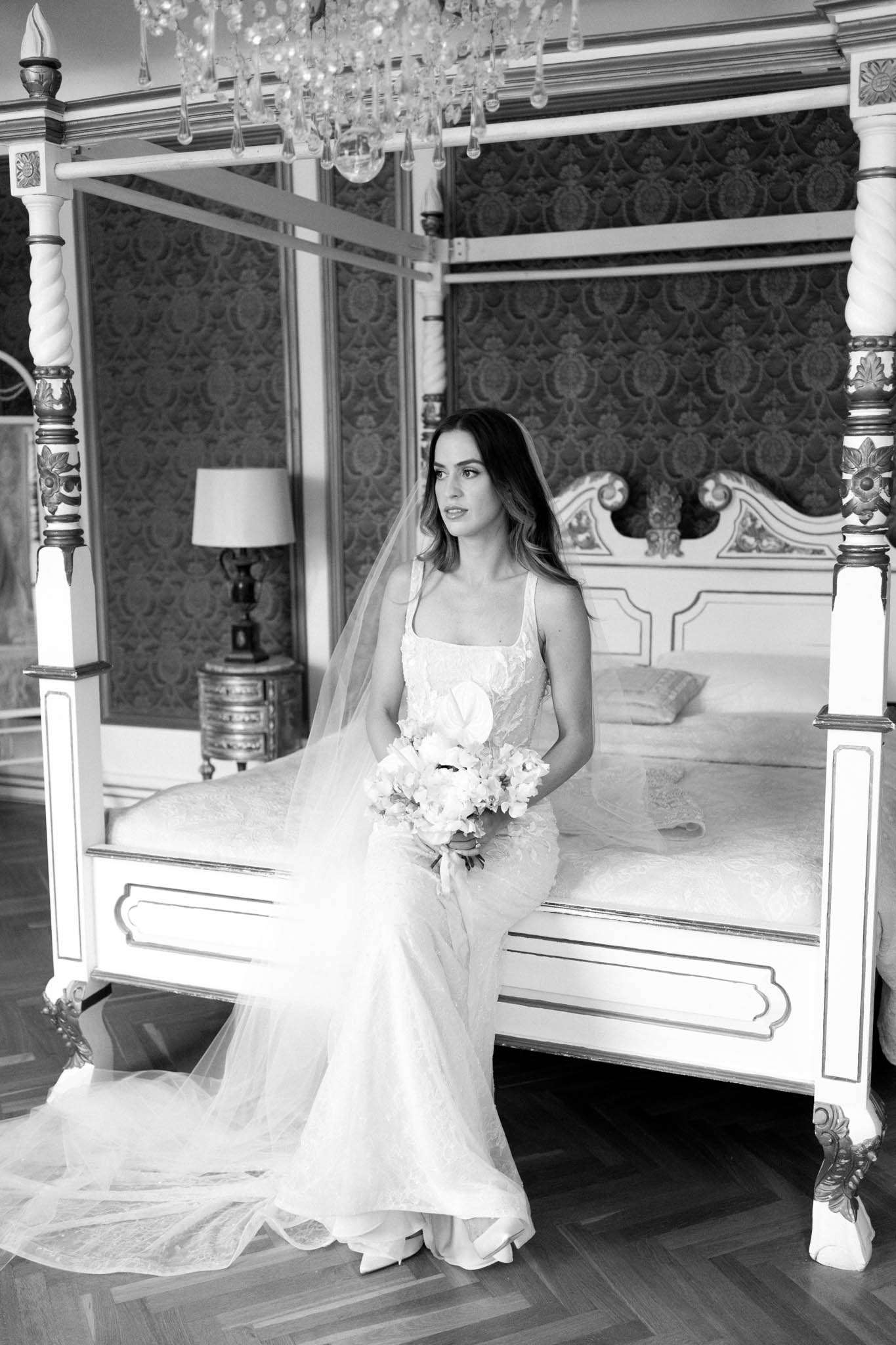 Black and white bridal portrait on four-poster bed in ornate chateau bedroom with cathedral veil