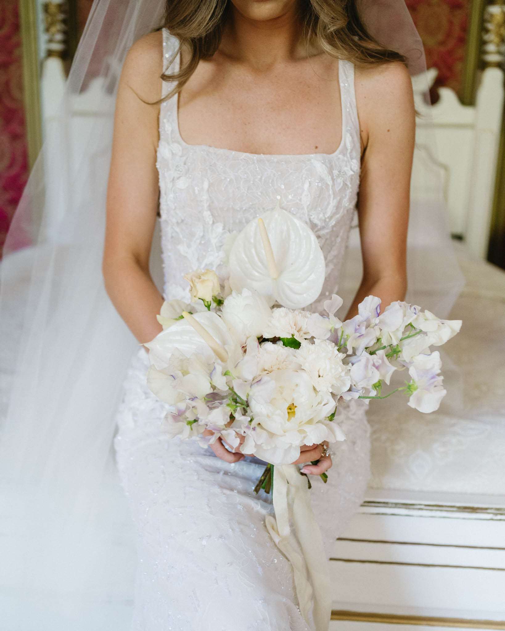 Close-up of bride holding anthurium, peony, and sweet pea bouquet in floral applique gown
