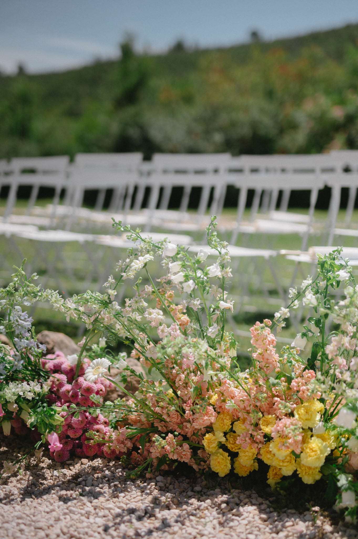Ground-level ceremony aisle florals with peach stock, yellow ranunculus, and pink celosia