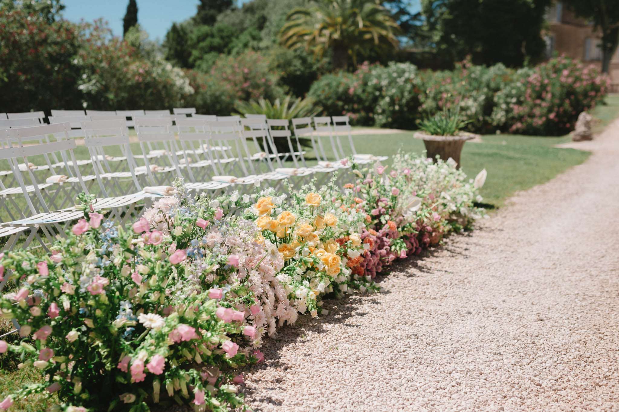 Pre-ceremony outdoor setup with white chairs and gradient ground-level floral aisle installation in garden
