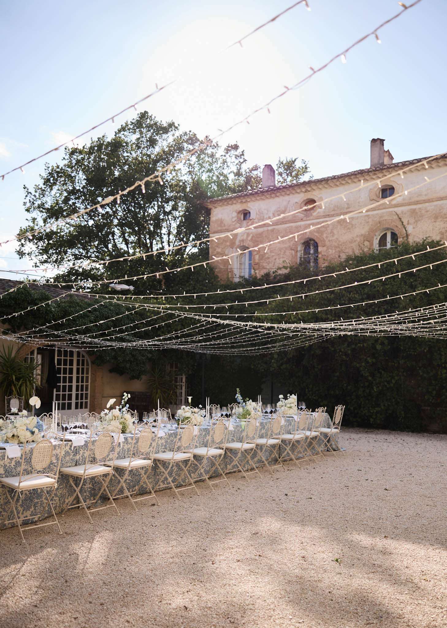 Blue toile tablecloths with white hydrangea centrepieces and fairy-light canopy at ochre stone courtyard