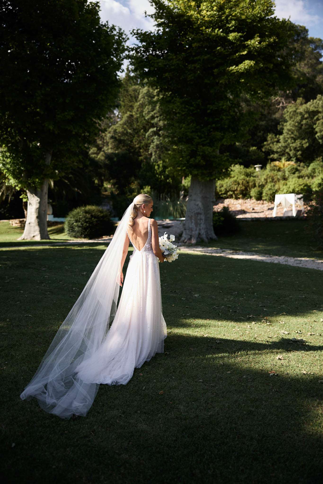 Bride in ivory A-line gown with cathedral veil and white bouquet on French estate lawn