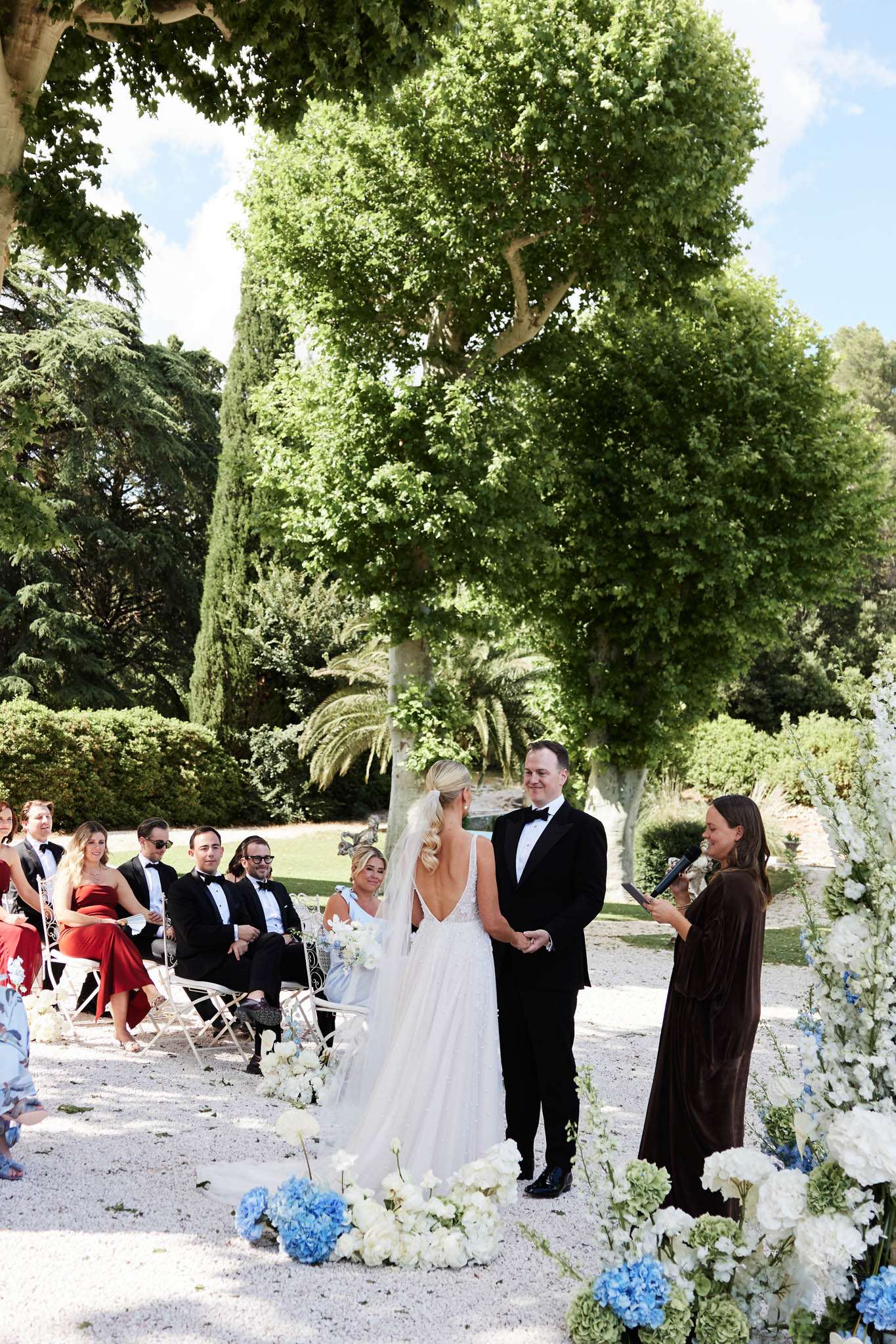 Couple at altar with white and blue hydrangea aisle arrangements and dozen guests in formal garden