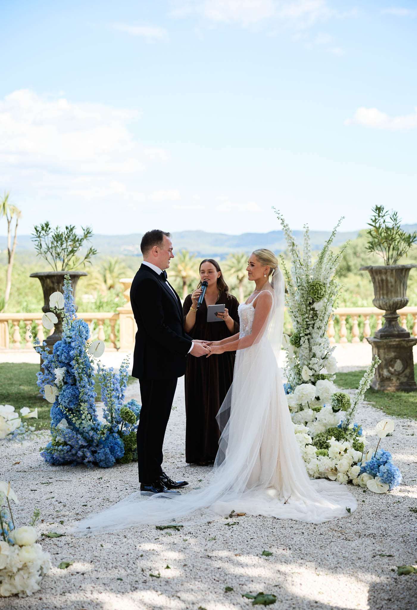 Outdoor ceremony on gravel terrace with blue delphinium and white hydrangea arrangements and mountain views