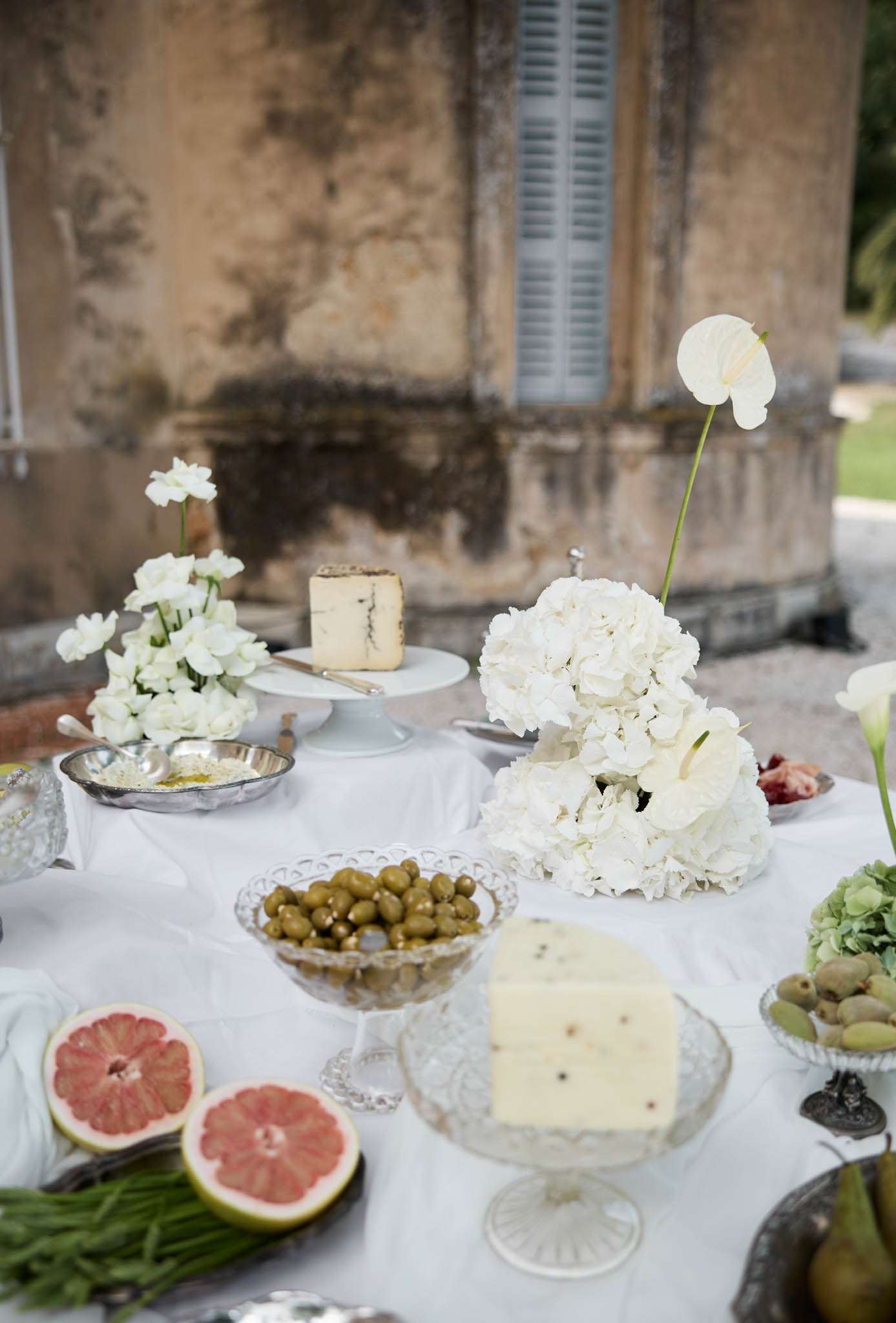 White cocktail food display with hydrangea arrangement, blue cheese, olives, and grapefruit at chateau facade