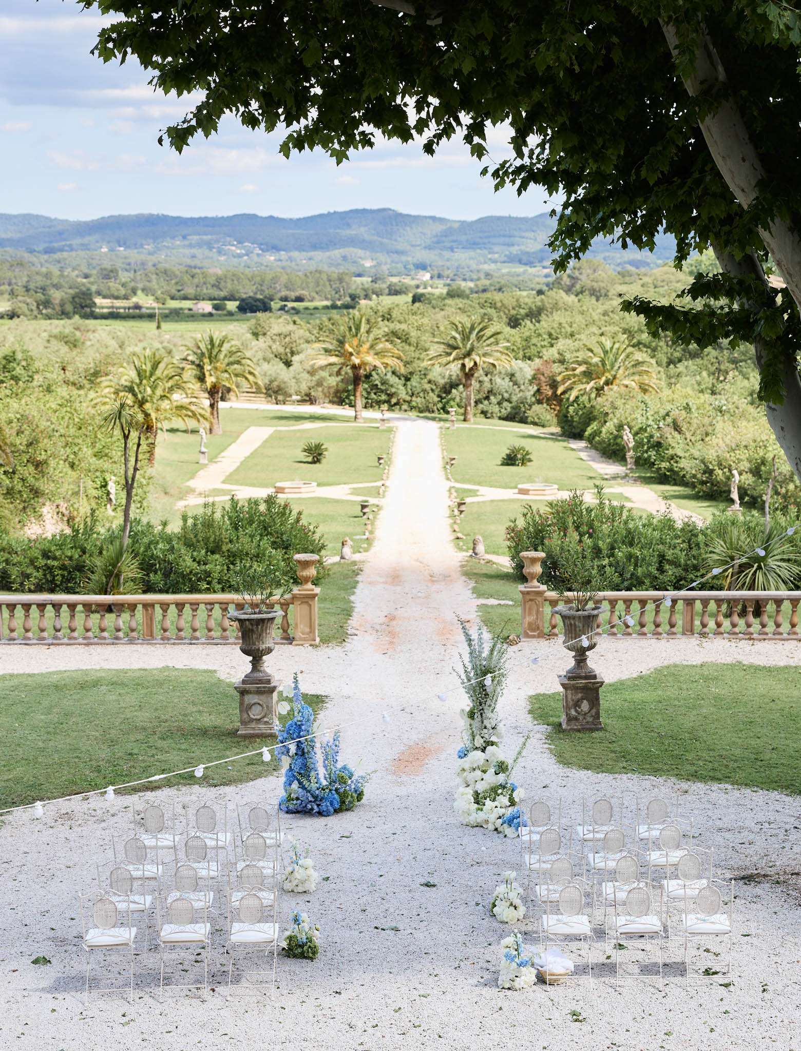 Elevated view ceremony setup ghost chairs blue delphinium and white hydrangea aisle florals before formal parterre garden