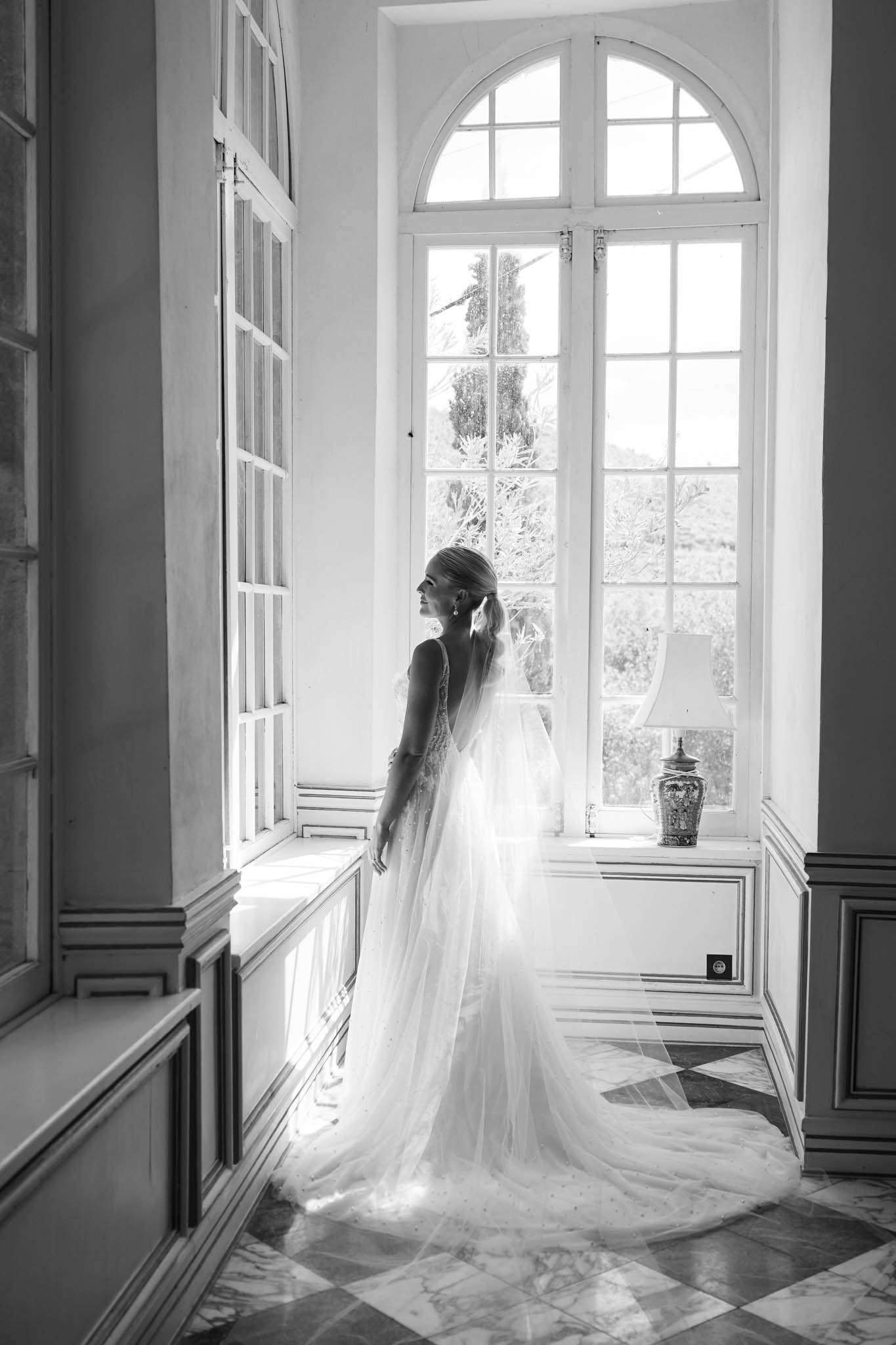 Black and white bride in tulle ballgown with cathedral train beside arched window in chateau