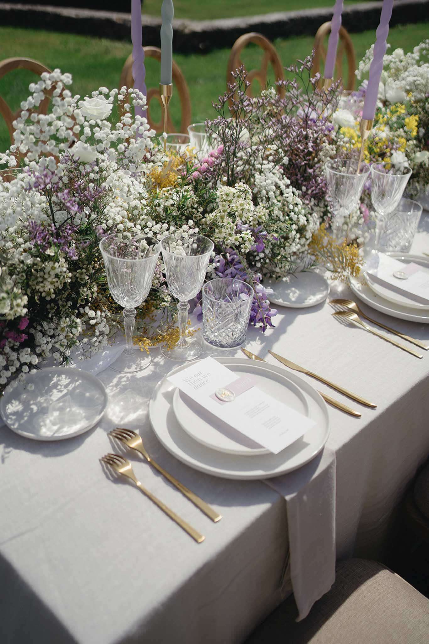 Outdoor reception table with wildflower garland of wisteria roses and mimosa lavender tapered candles and gold flatware