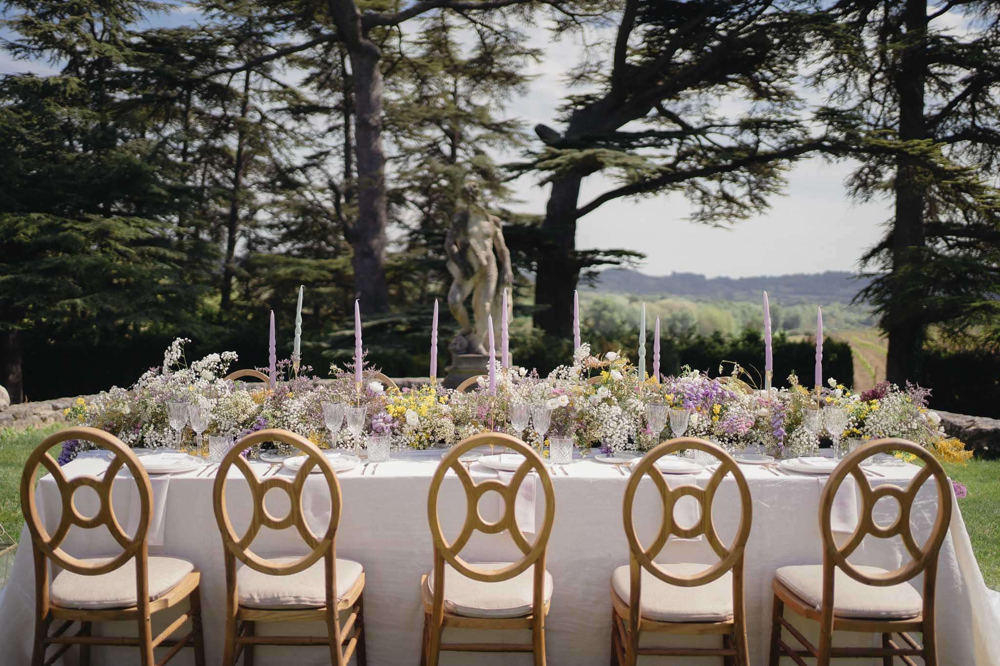 Long table with gypsophila, lavender blooms, and sage tapers in geometric-back chairs on chateau lawn