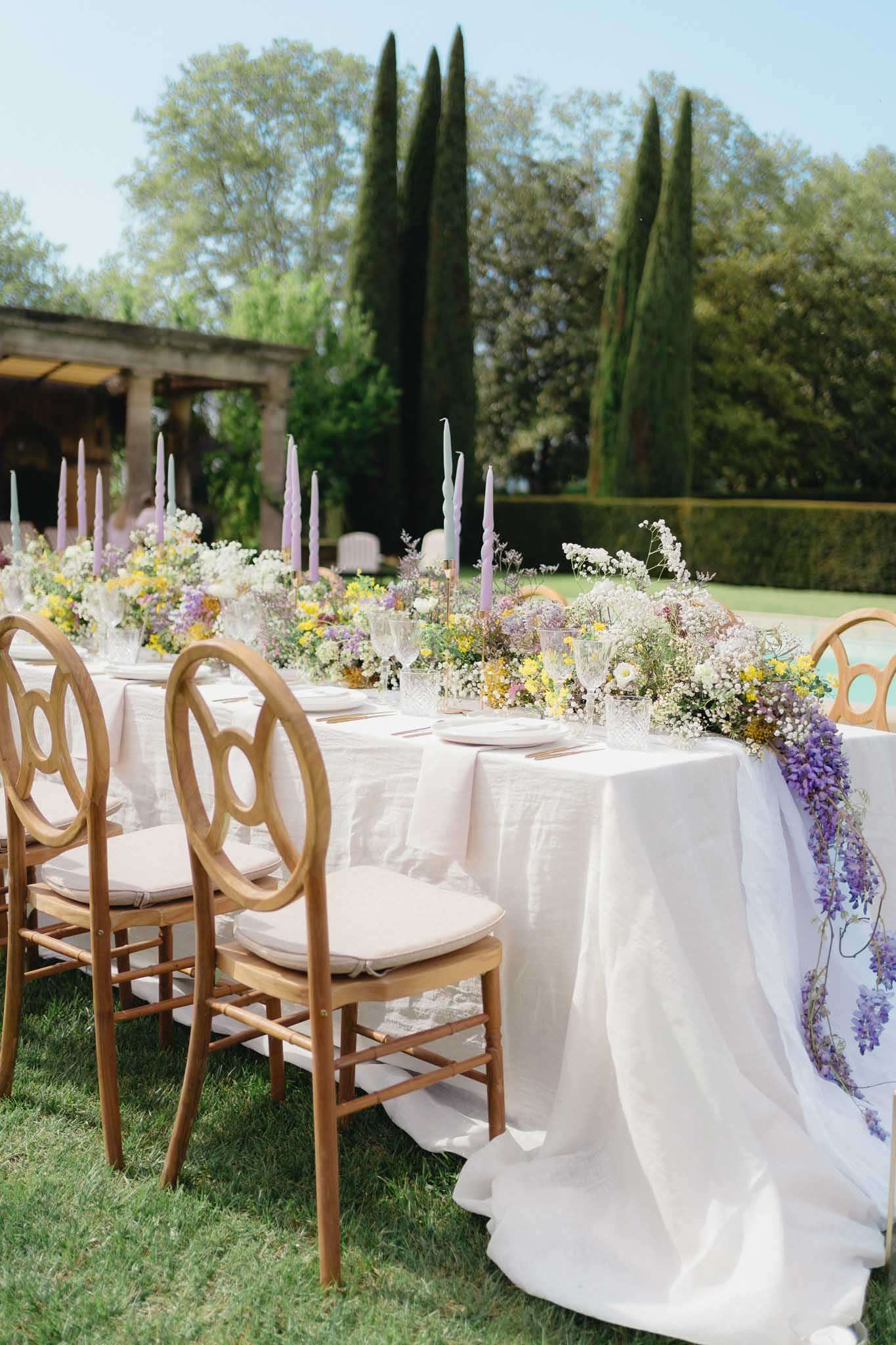 Reception table with wildflower runner of baby's breath, yellow blooms, and purple wisteria with lavender candles