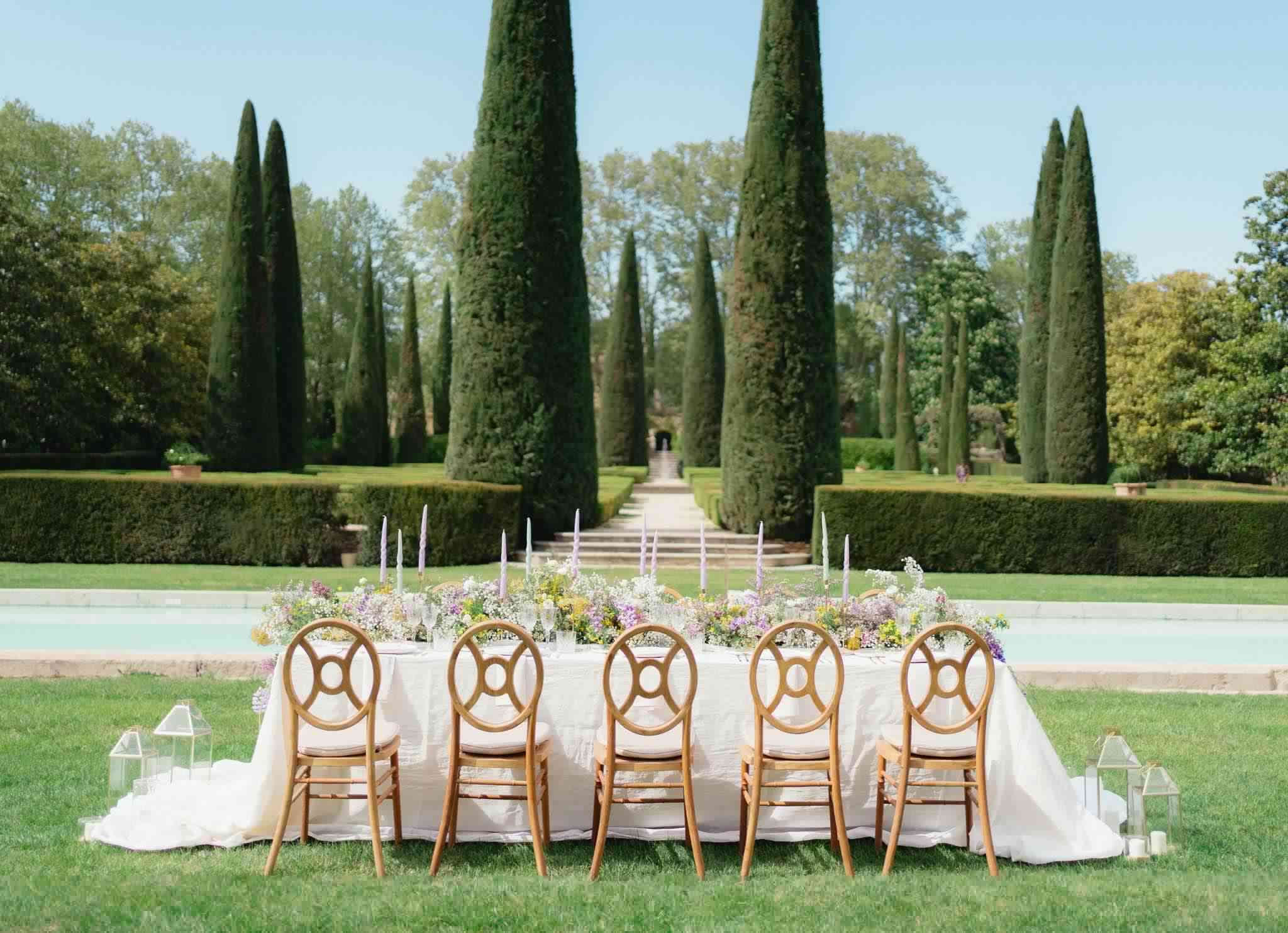 Ivory table with lavender taper candles and wildflower runner in formal cypress-lined garden with pool