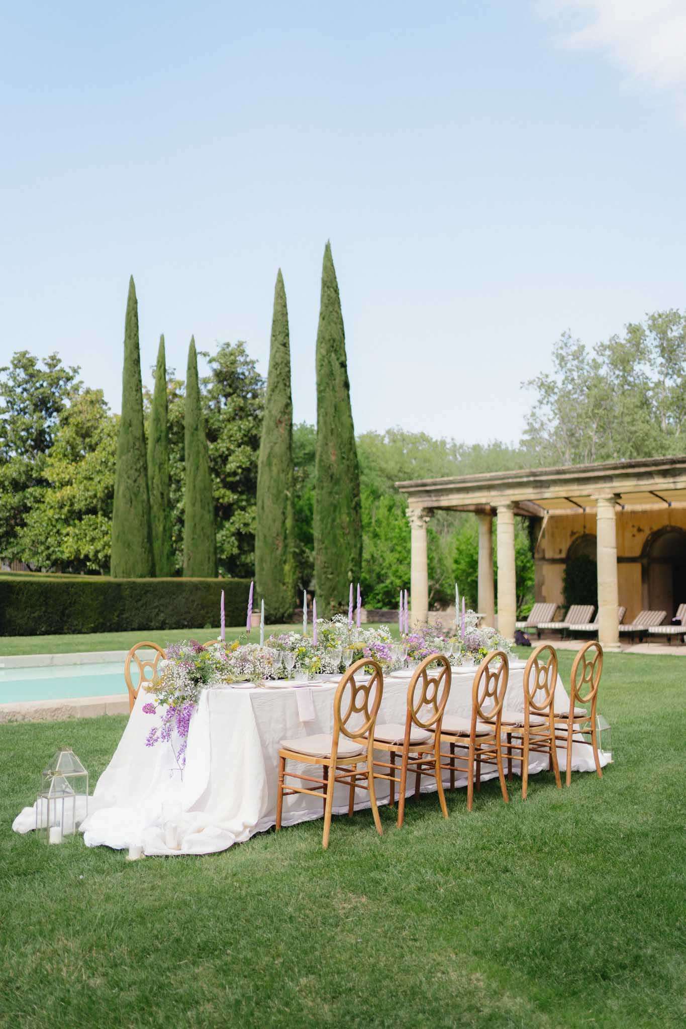 Outdoor reception table on lawn beside pool at French chateau with wisteria and lavender taper candle centerpieces