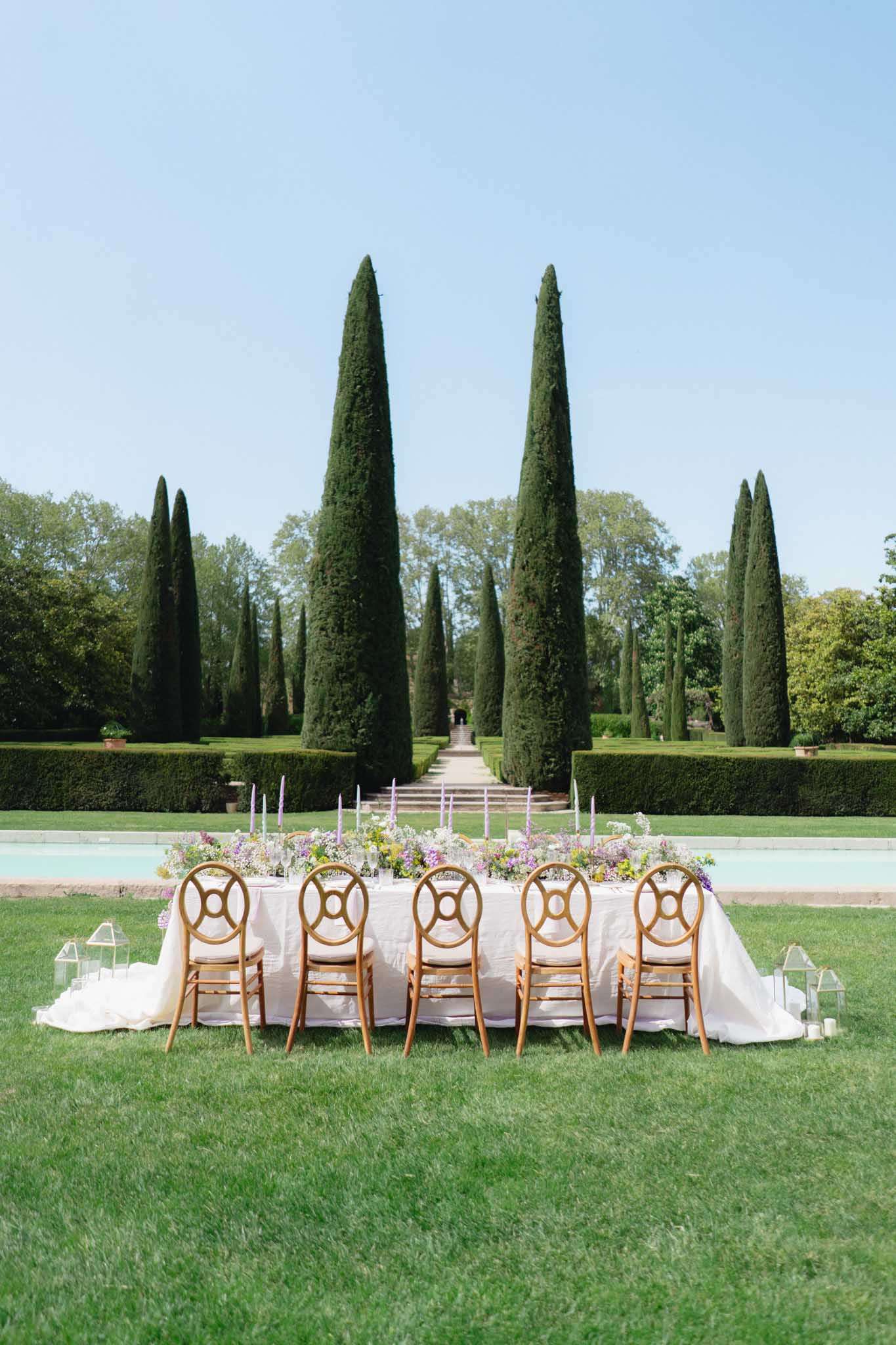 Long table with lilac wildflower runner and lavender tapers before cypress allee and reflecting pool