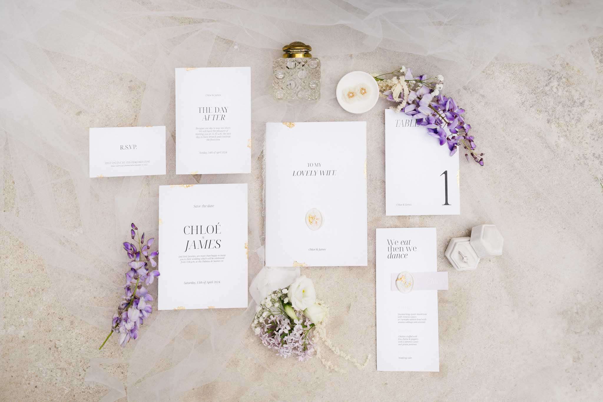 Gold foil stationery suite with velvet ring box, wisteria sprigs, and crystal perfume on stone