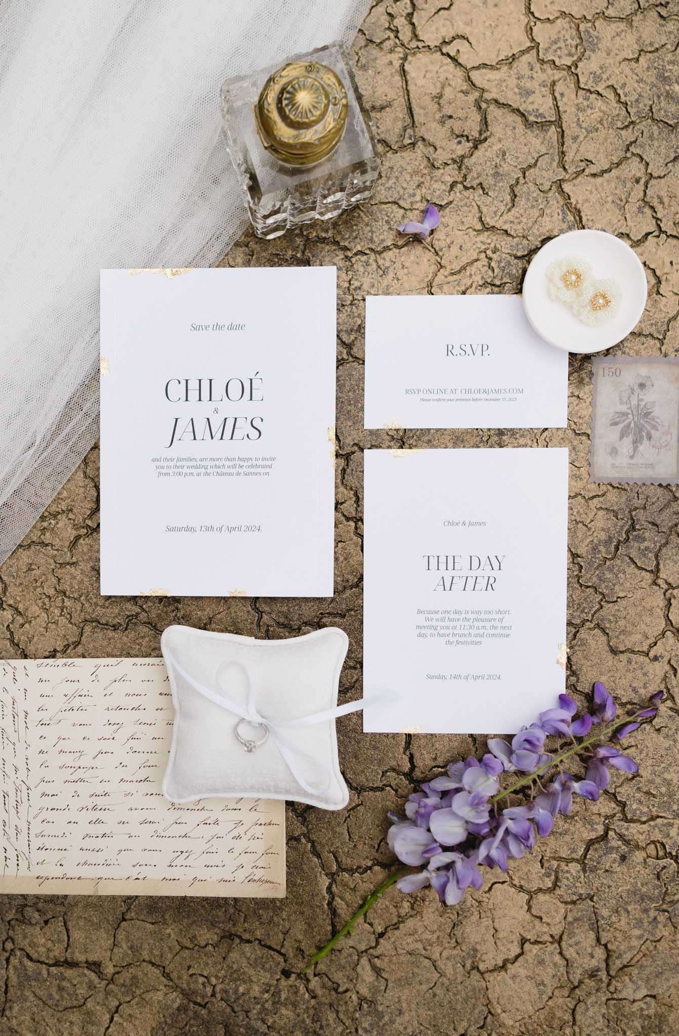 Flat lay of wedding stationery suite with gold foil details, engagement ring, pearl earrings, and wisteria sprig