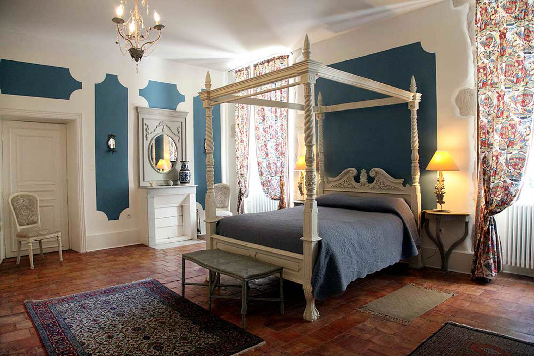 Chateau bedroom with carved four-poster bed slate blue quilt teal panels Persian rug and wrought iron chandelier