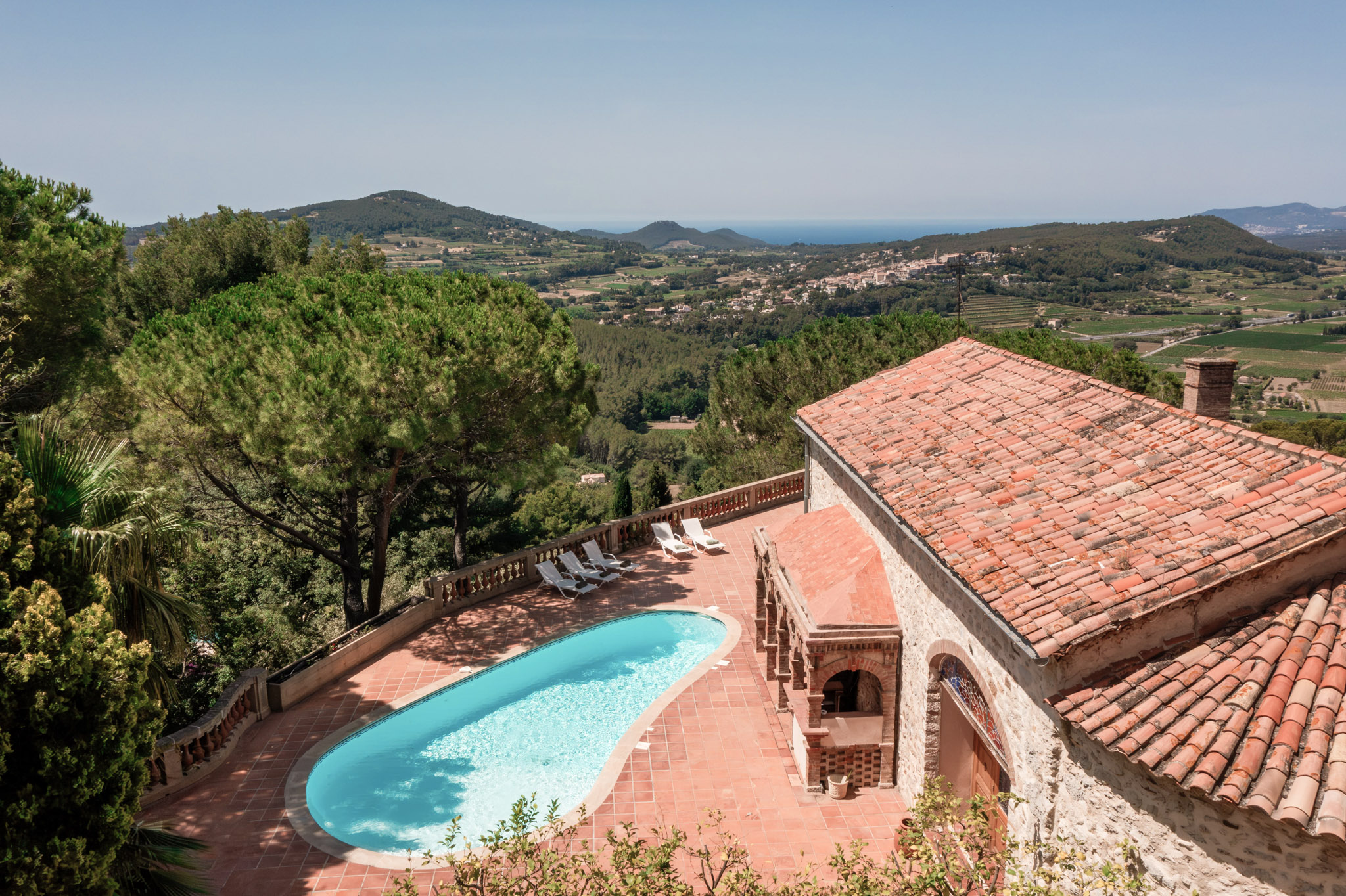 Aerial view of Provencal stone villa with oval pool on hillside terrace overlooking sea and valley
