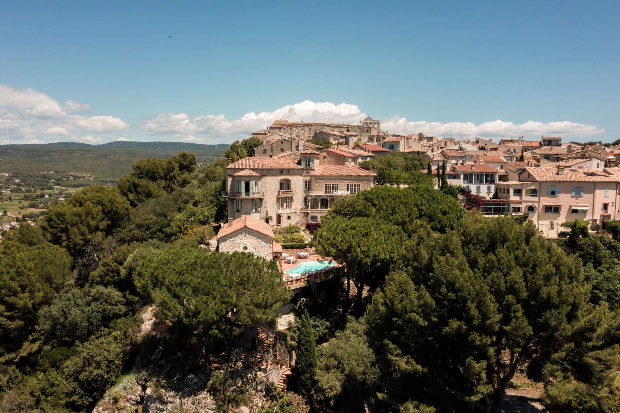Aerial view of Provencal hilltop village with stone manor, chapel, pool, and round reception tables