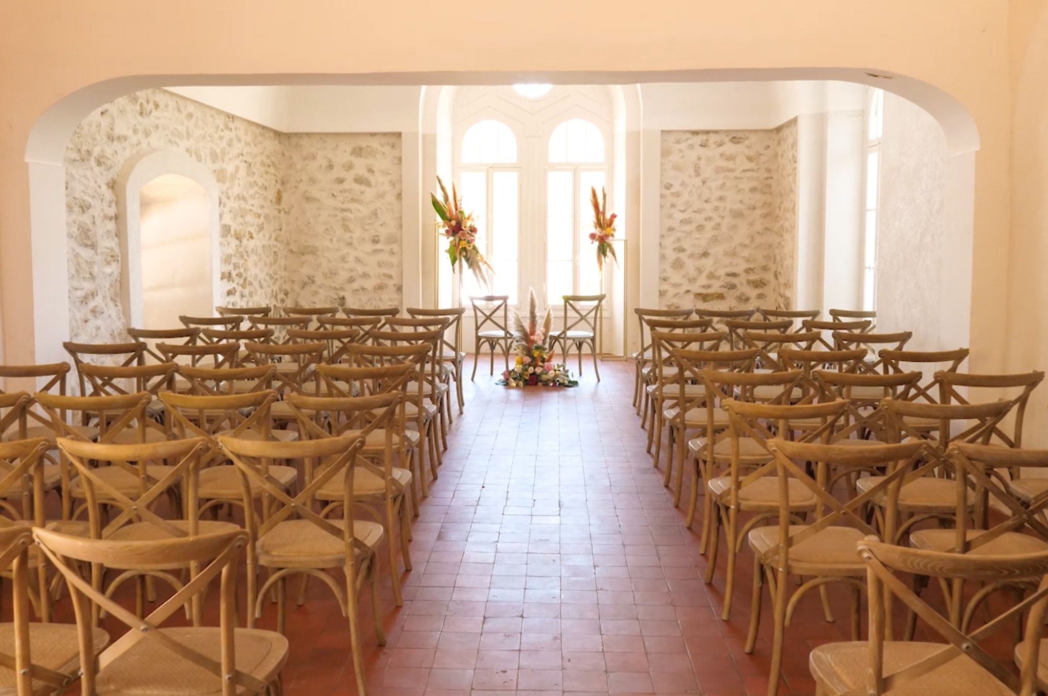 Stone-walled ceremony room with cross-back chairs and coral tropical floral arrangements at the altar end