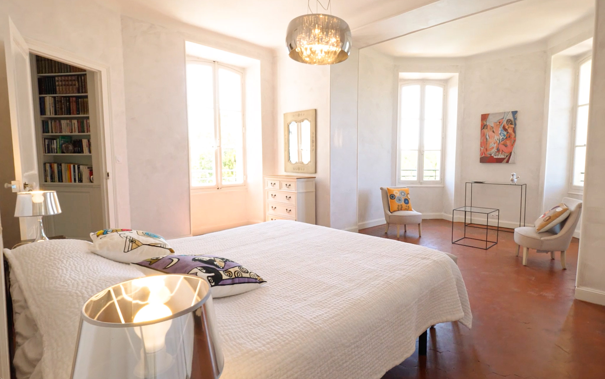 Chateau bedroom with white quilted bed, chrome chandelier, terracotta floors, and modern furnishings