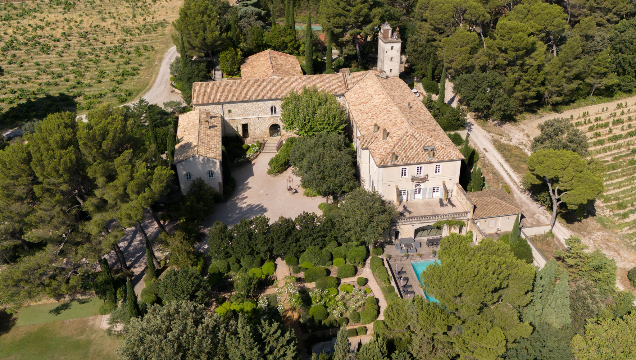 Aerial view of stone chateau with terracotta roofs, parterre garden, swimming pool, and surrounding vineyards