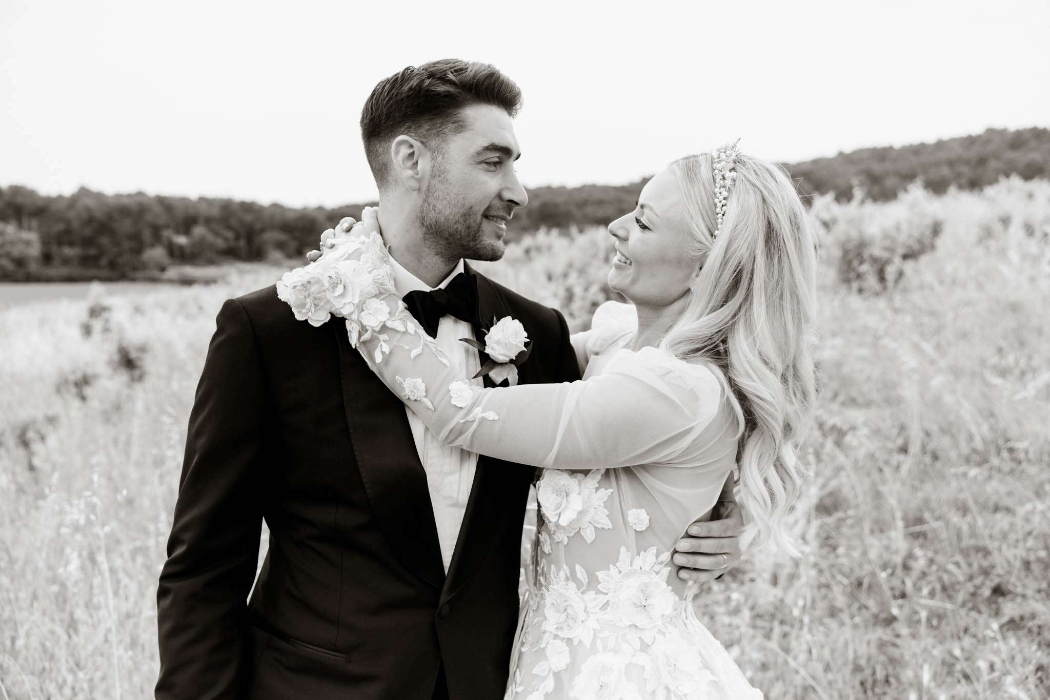 Black and white close-up of couple smiling in field with floral applique gown and embellished headband