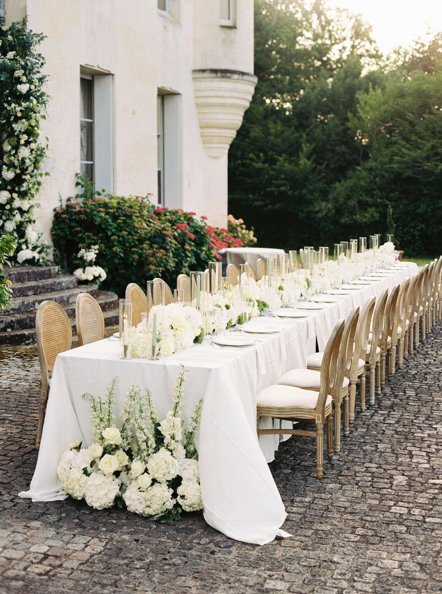 All-white hydrangea and rose runner on long table with gold Louis XVI chairs at chateau courtyard