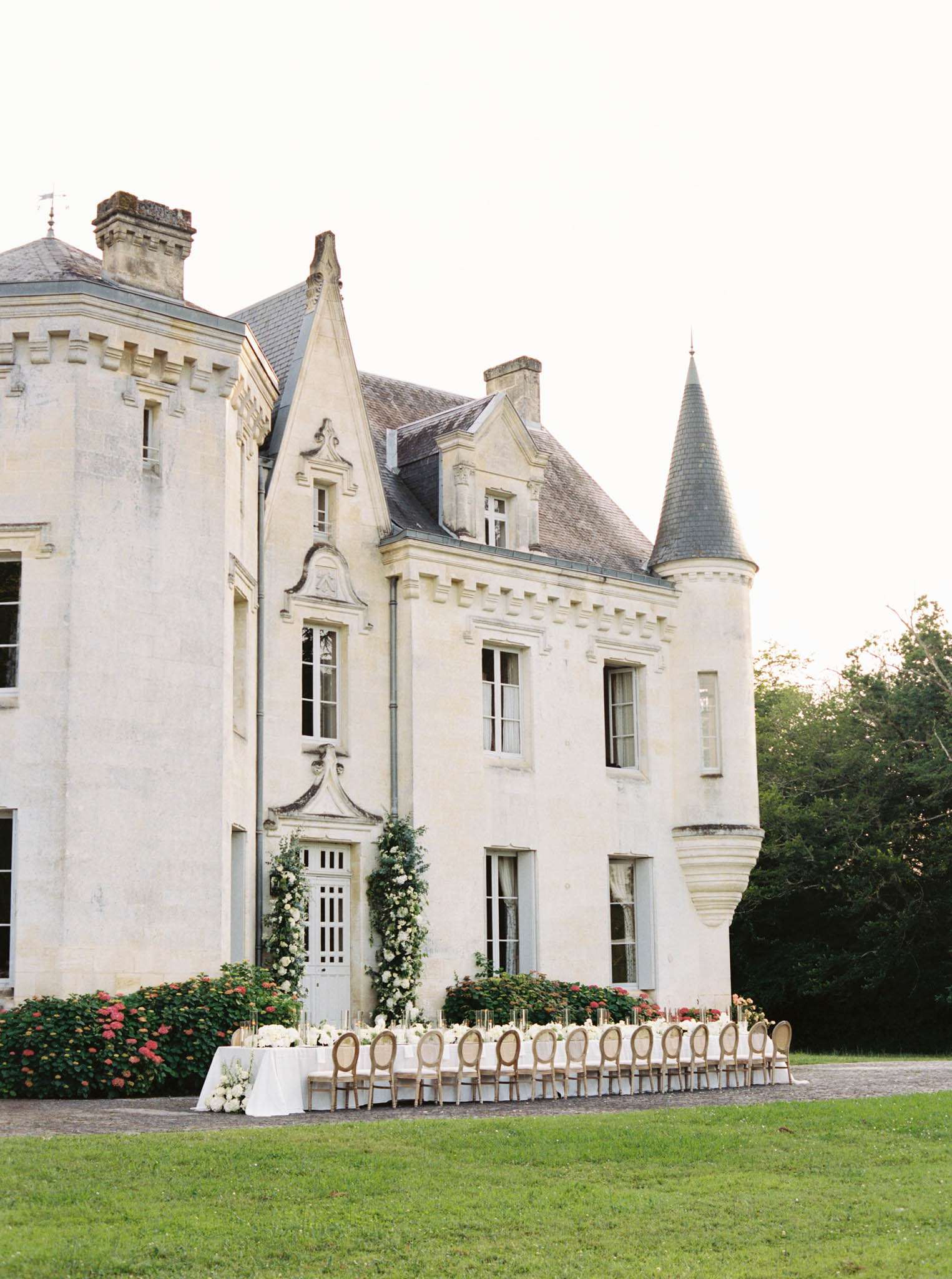 Banquet table with gold candles and cane-back chairs before turreted chateau with climbing floral doorway