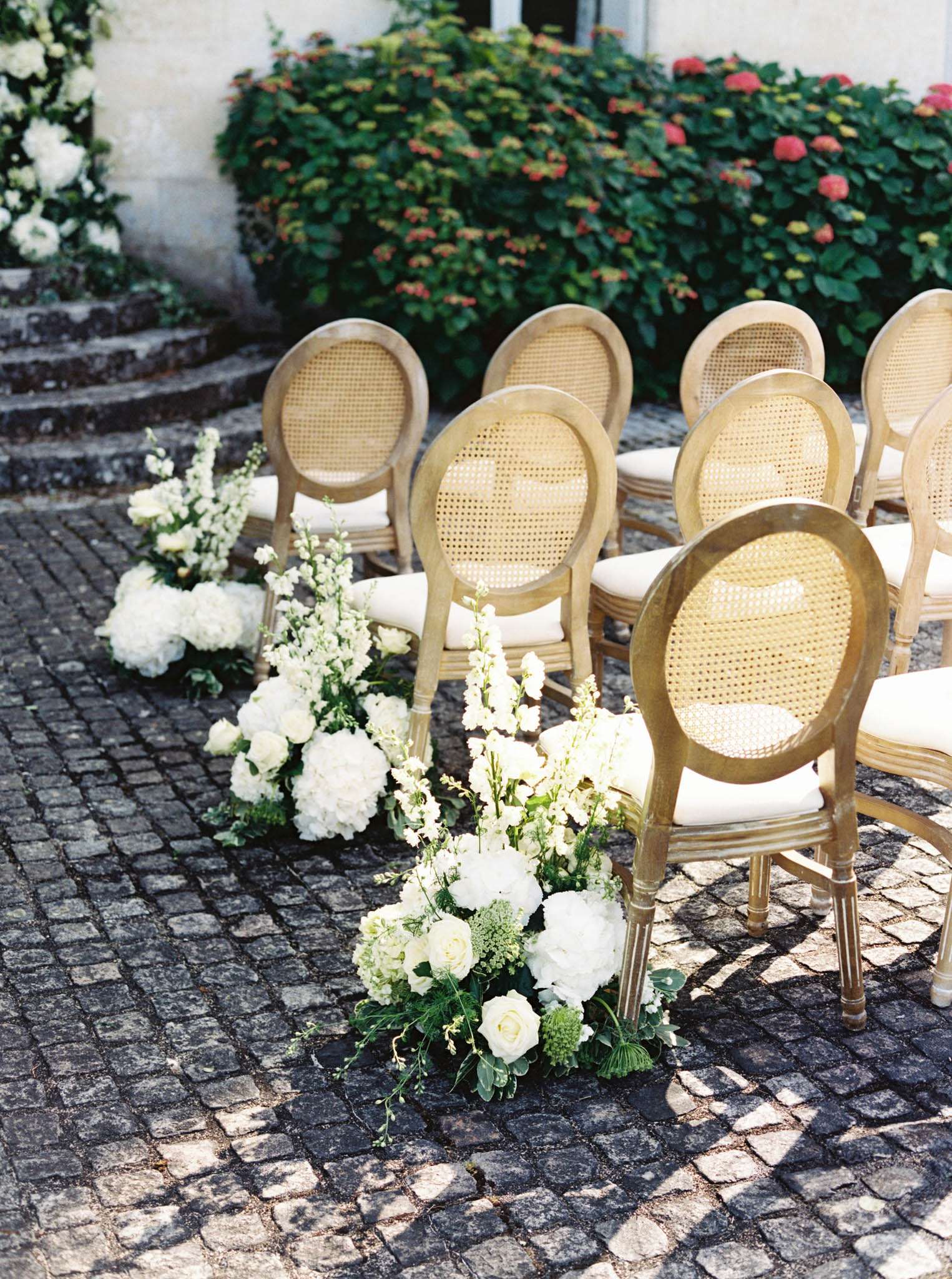 Ceremony aisle on chateau cobblestone courtyard with gold Louis XVI chairs and white hydrangea and rose arrangements