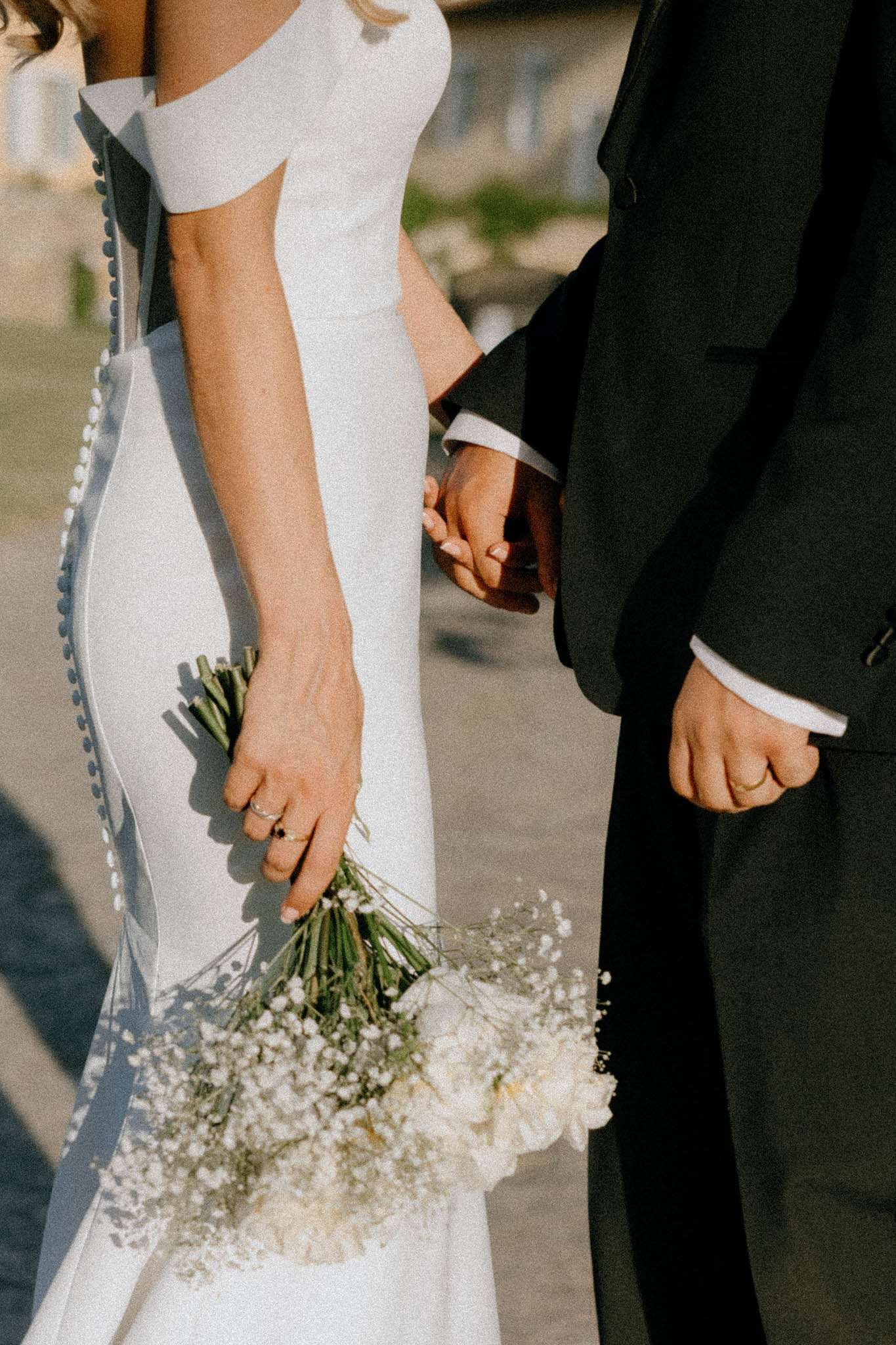 Close-up of bride and groom holding hands, bride carrying white gypsophila bouquet with blue ribbon detail